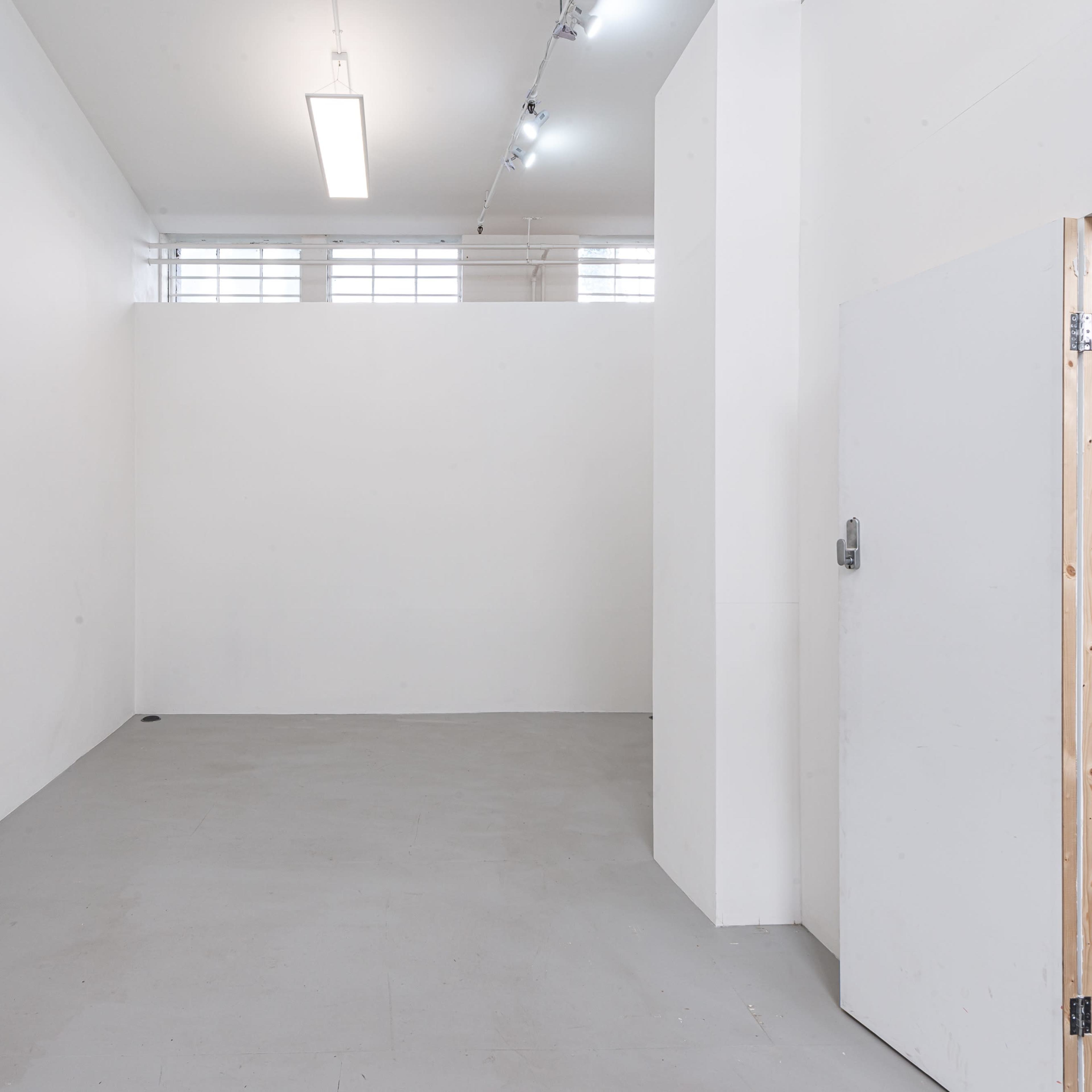 An empty, white-walled interior space with a concrete floor and a doorway on the right.