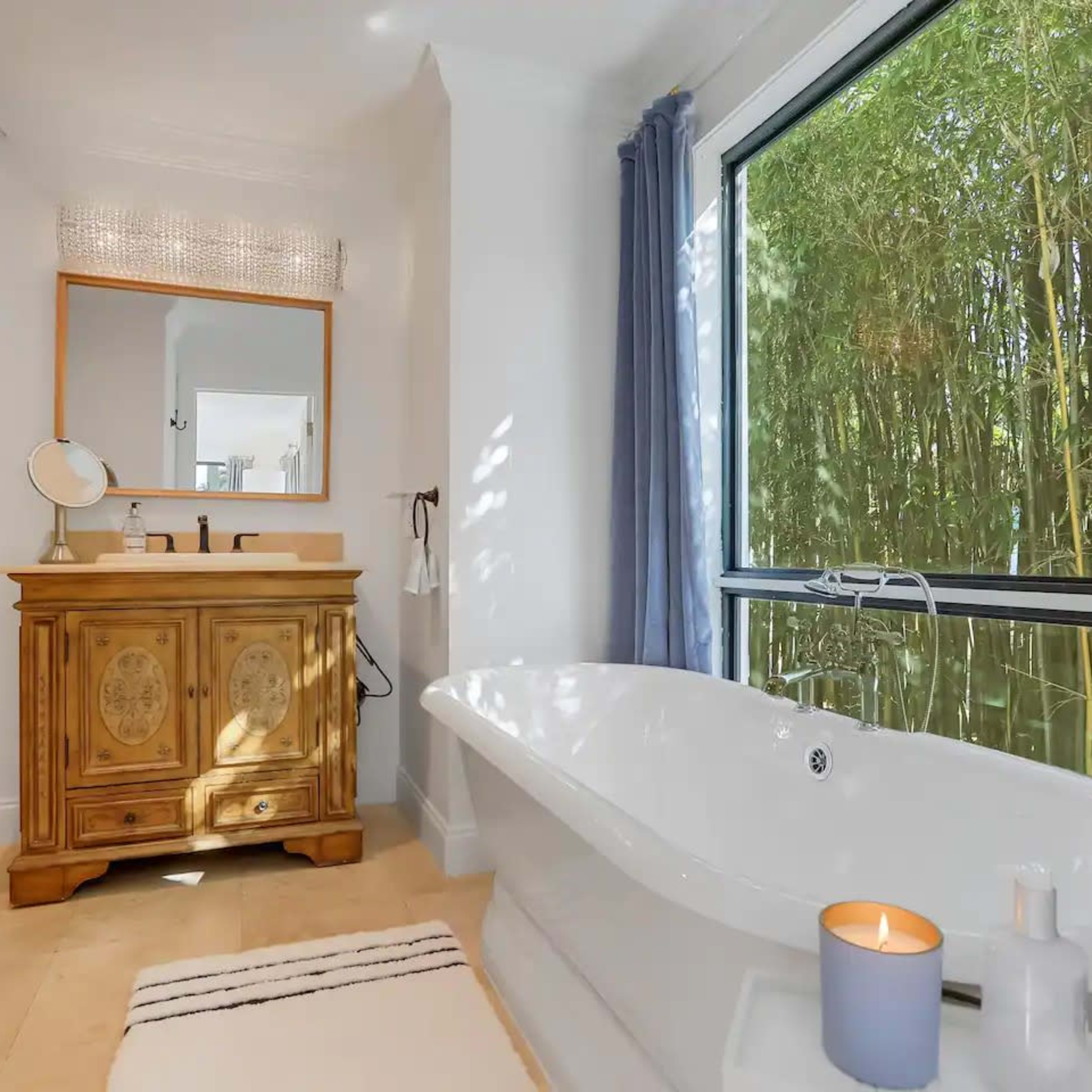 A bright bathroom featuring a freestanding bathtub, a wooden vanity, and large windows overlooking a bamboo grove.
