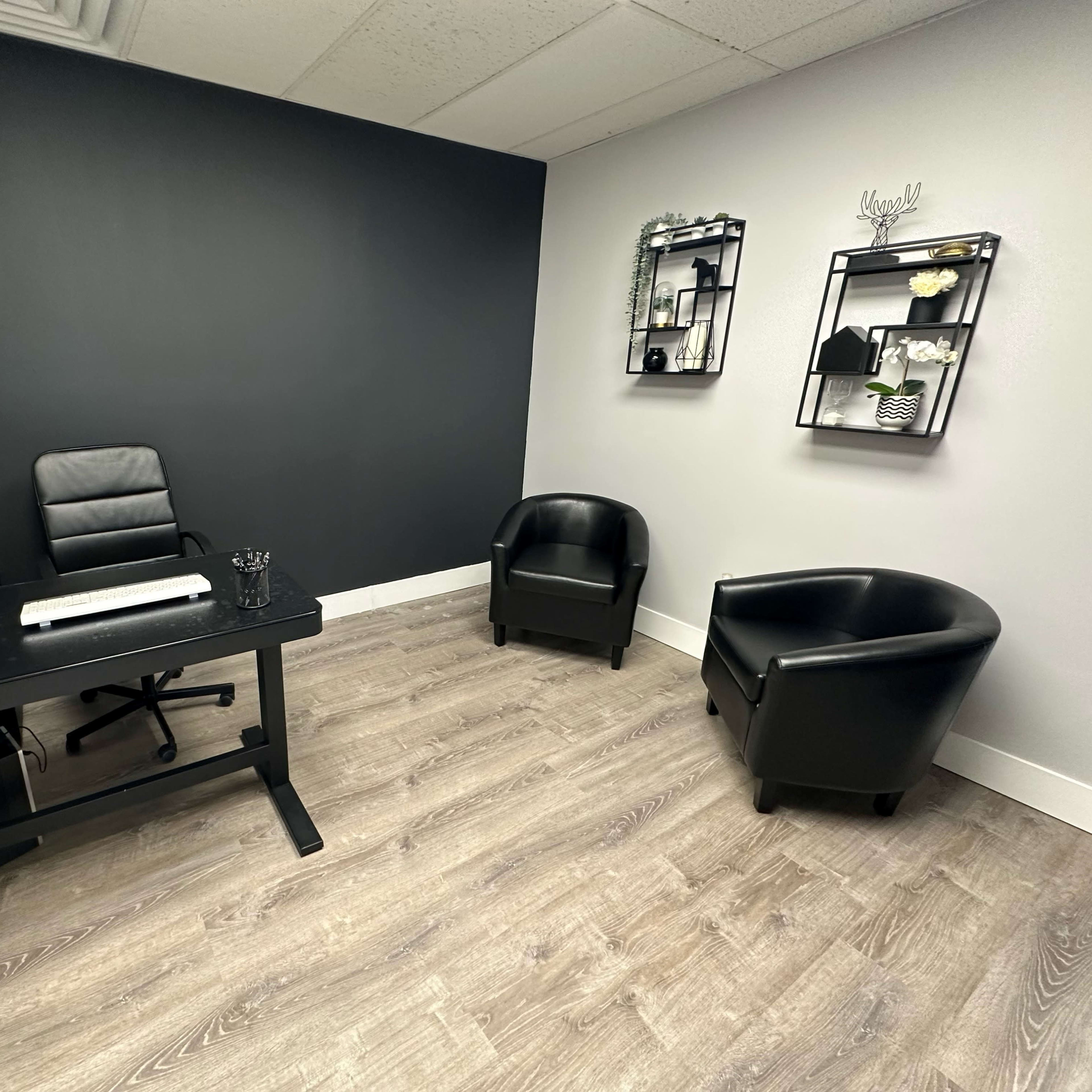 A modern office space with a desk, a black chair, and two black armchairs against a dark gray wall.