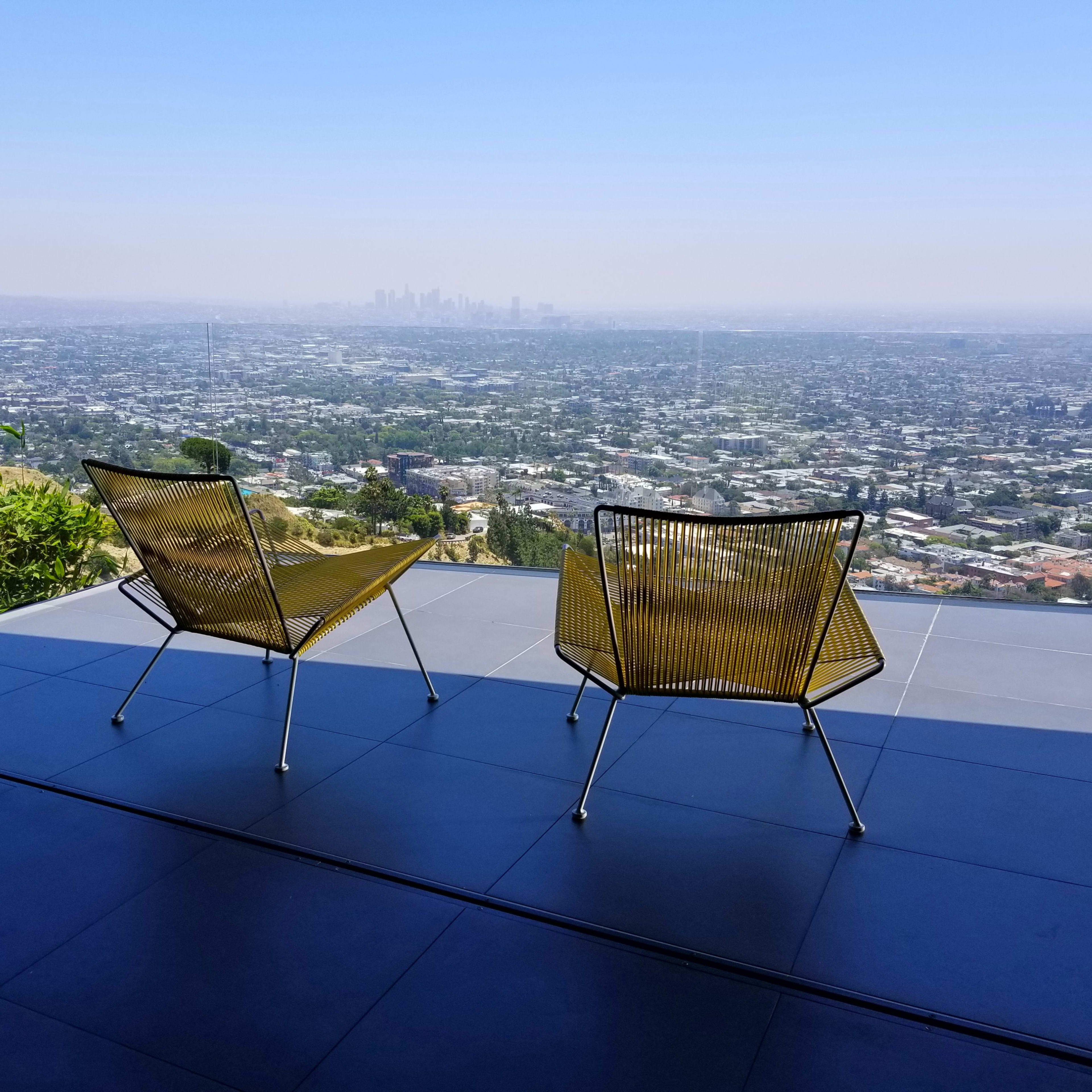 Two yellow wire chairs are positioned on a patio overlooking a sprawling view of a cityscape.