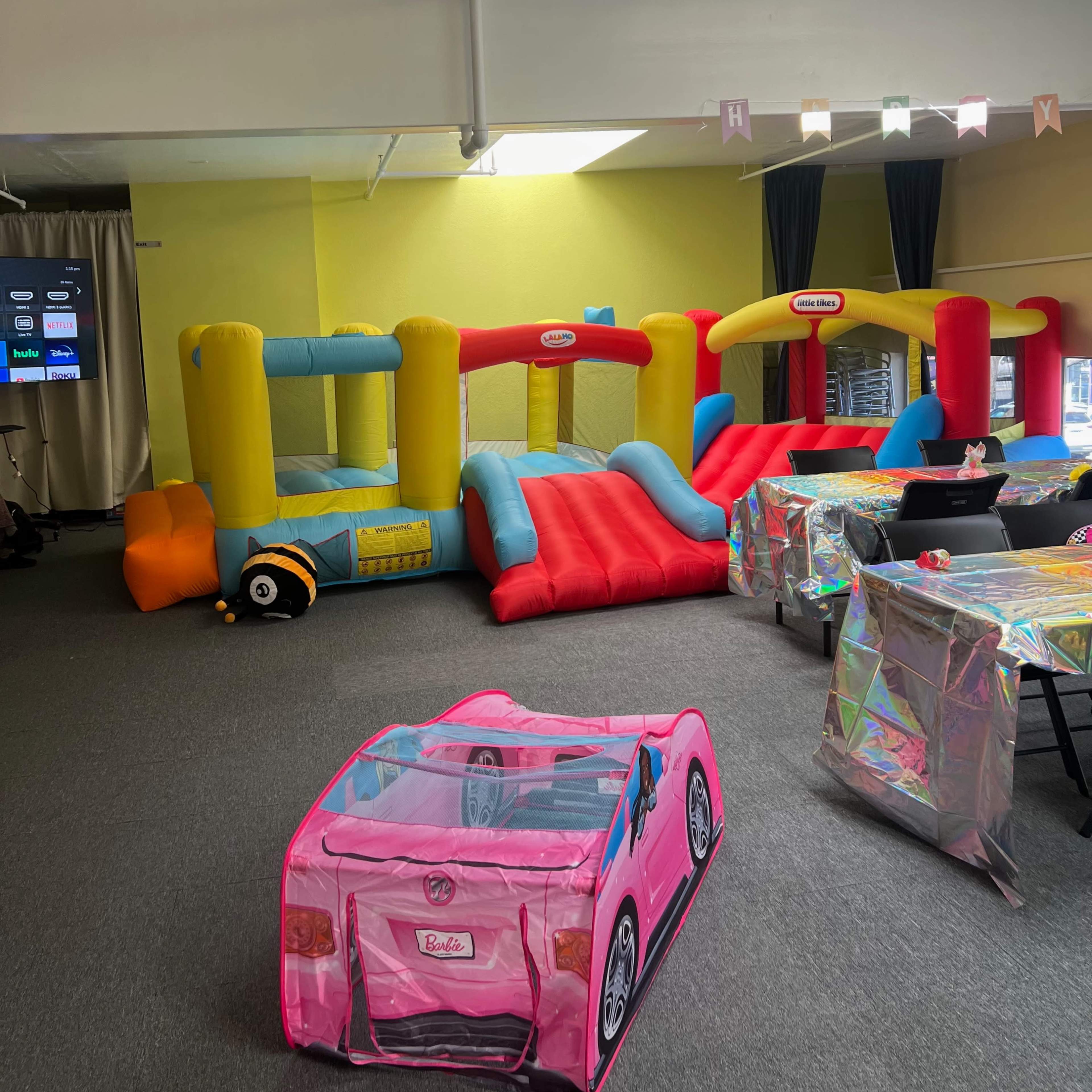A party room featuring colorful inflatable play structures and a toy car, with tables set up nearby.