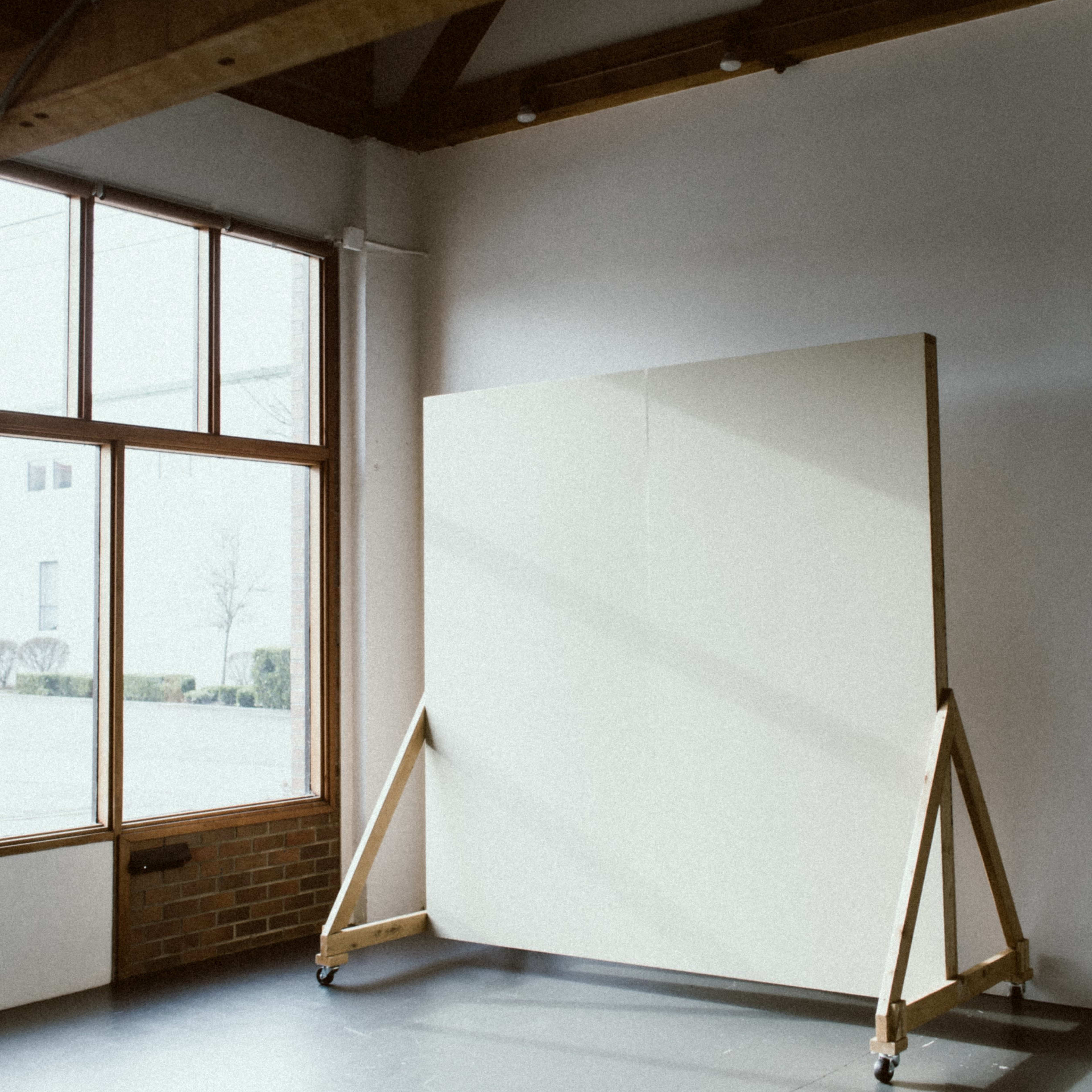 A spacious room with large windows and a blank canvas mounted on a wooden easel.