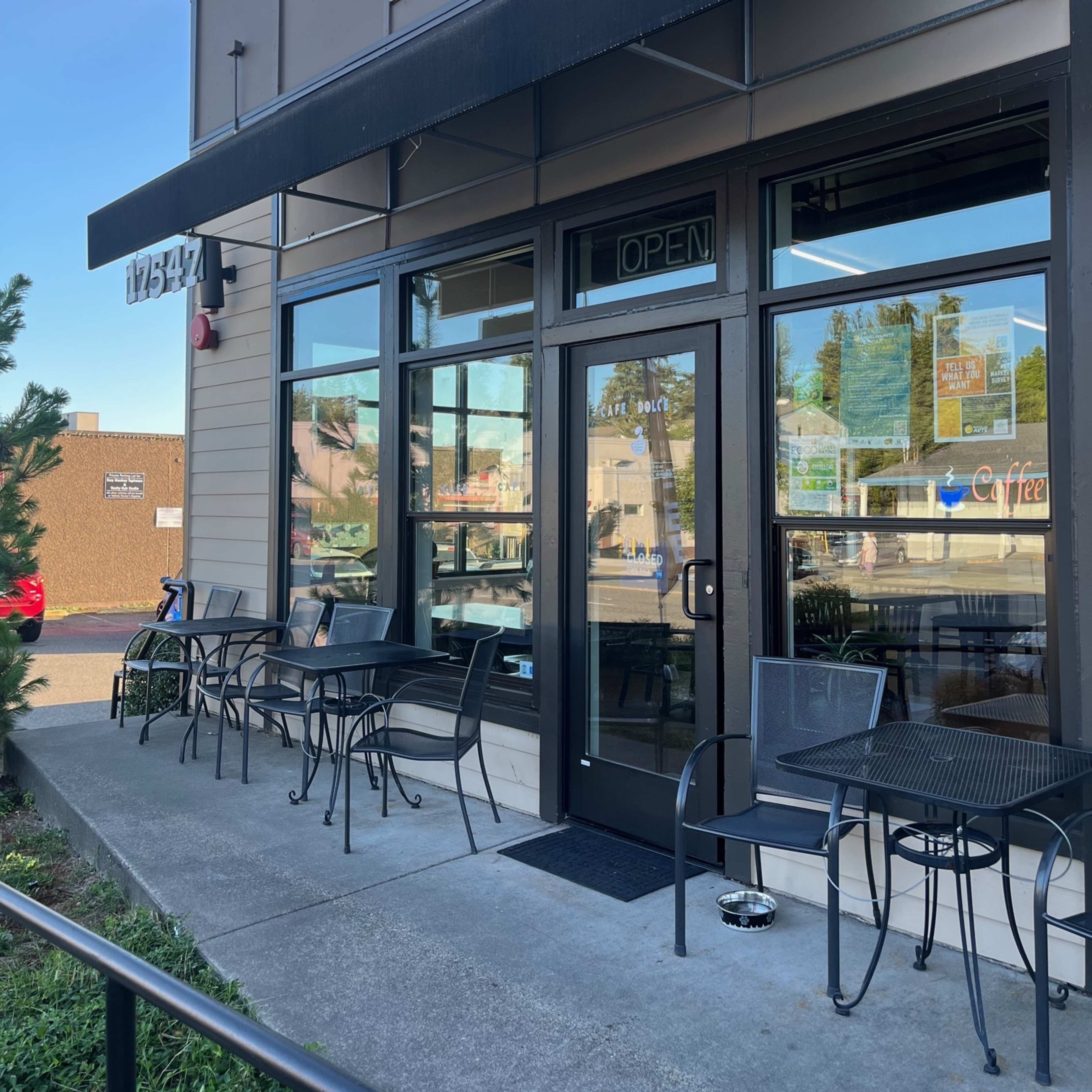 The entrance of Café Dolce, featuring a black awning, glass doors, and several outdoor tables along the sidewalk.
