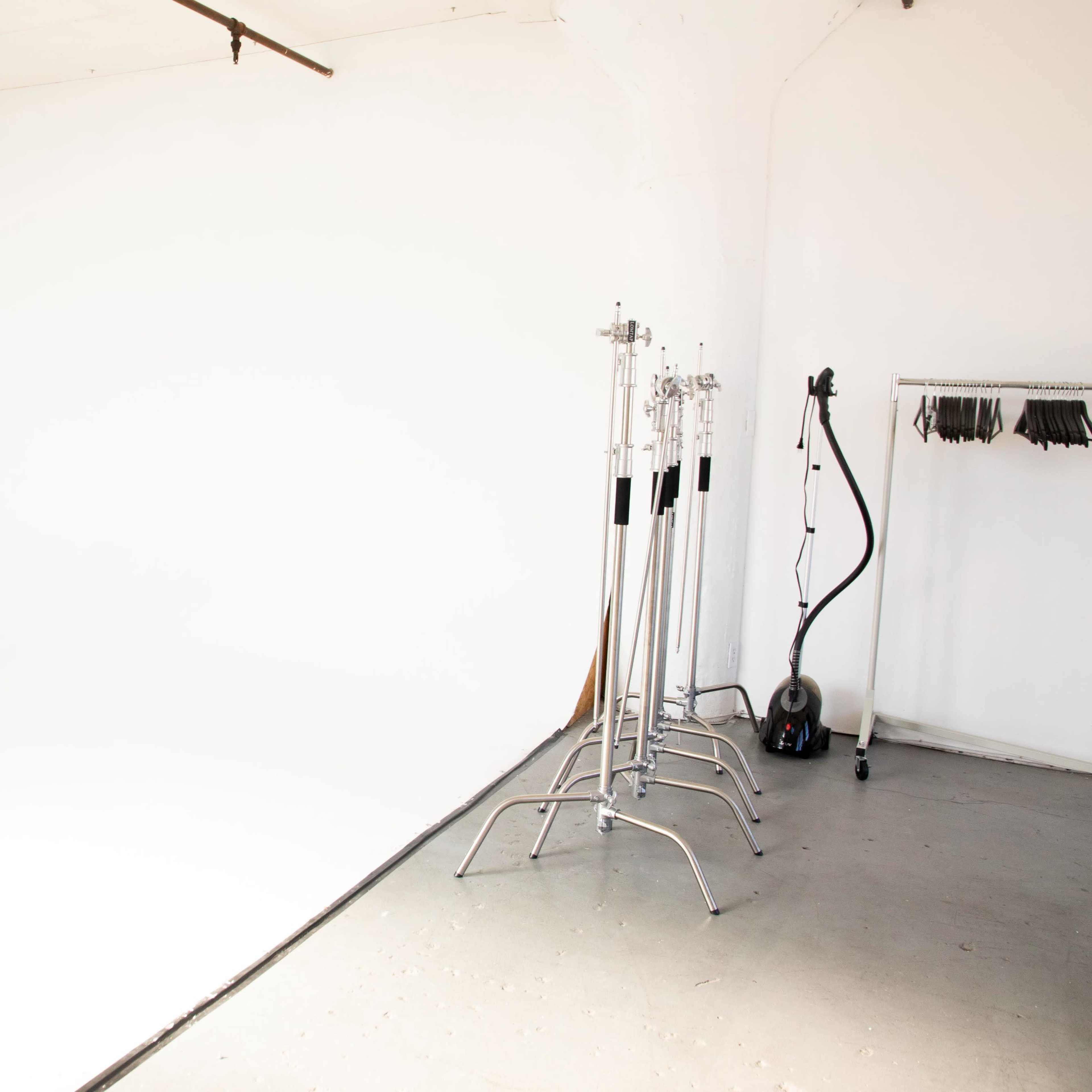 A spacious studio with a white backdrop, photography stands, and a clothing rack on the right.