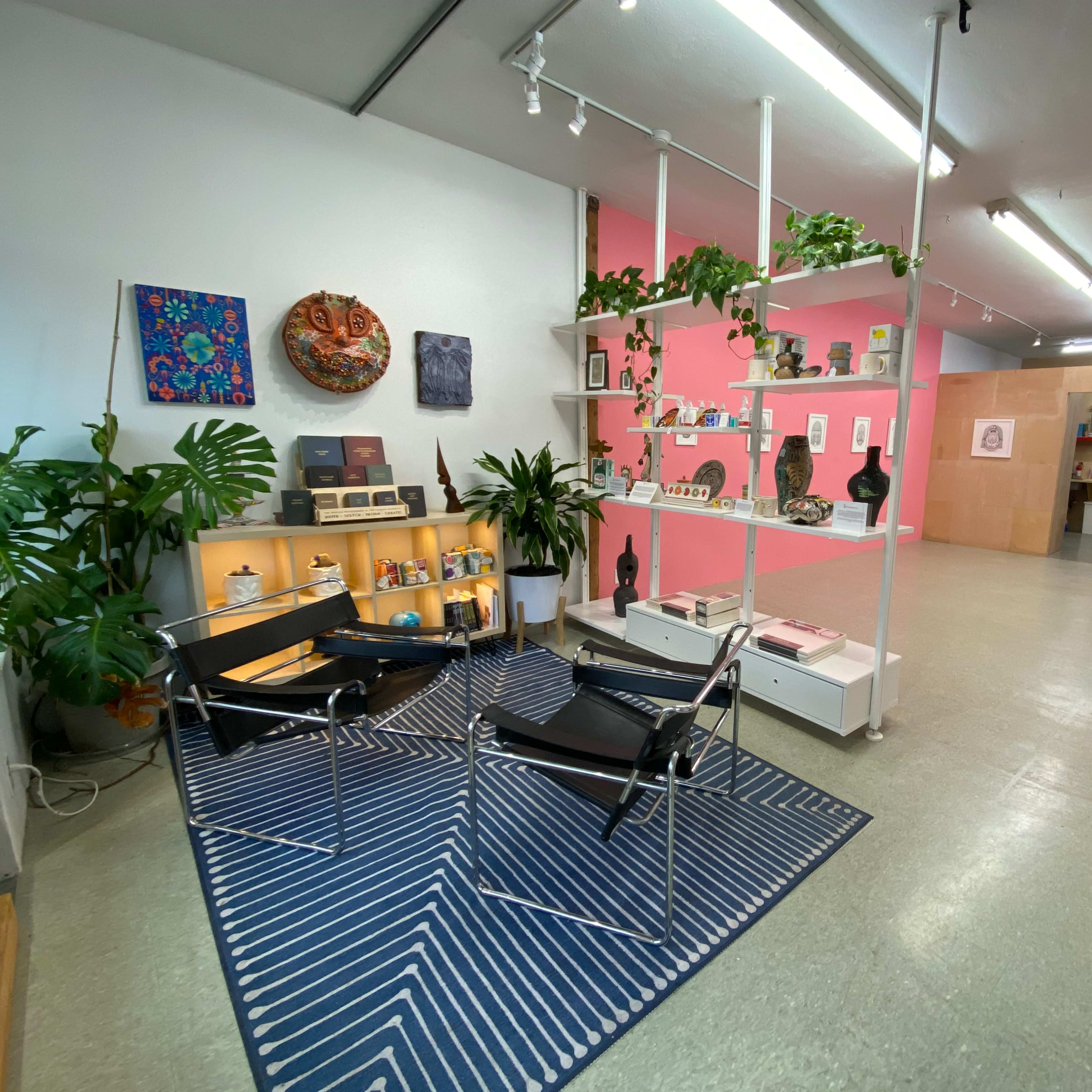 A modern, spacious interior with seating, decorative plants, art displays on the walls, and a dividing wall leading to another area.