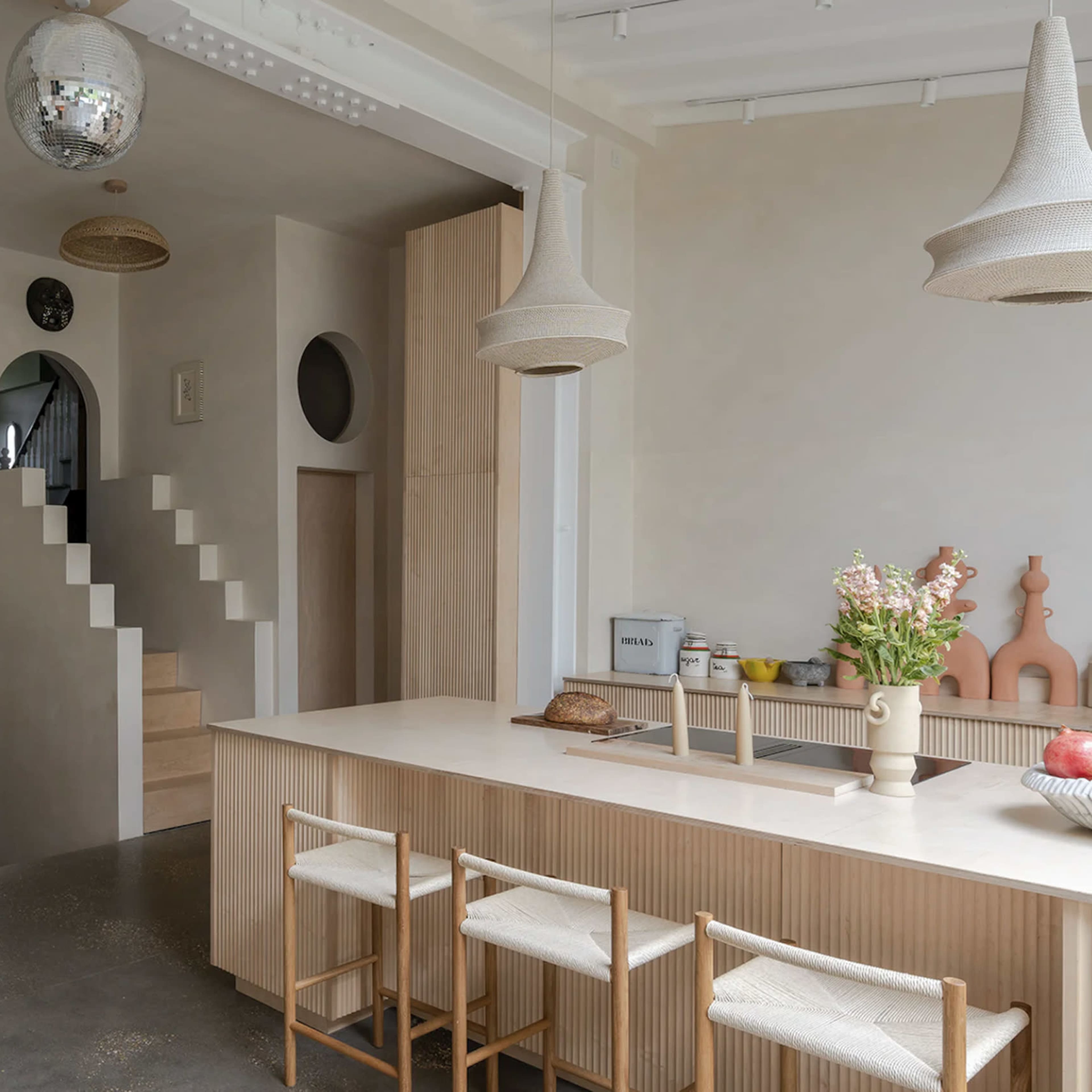 A modern, open-concept living space featuring a kitchen island with seating, a staircase, and a cozy sitting area with a circular rug.