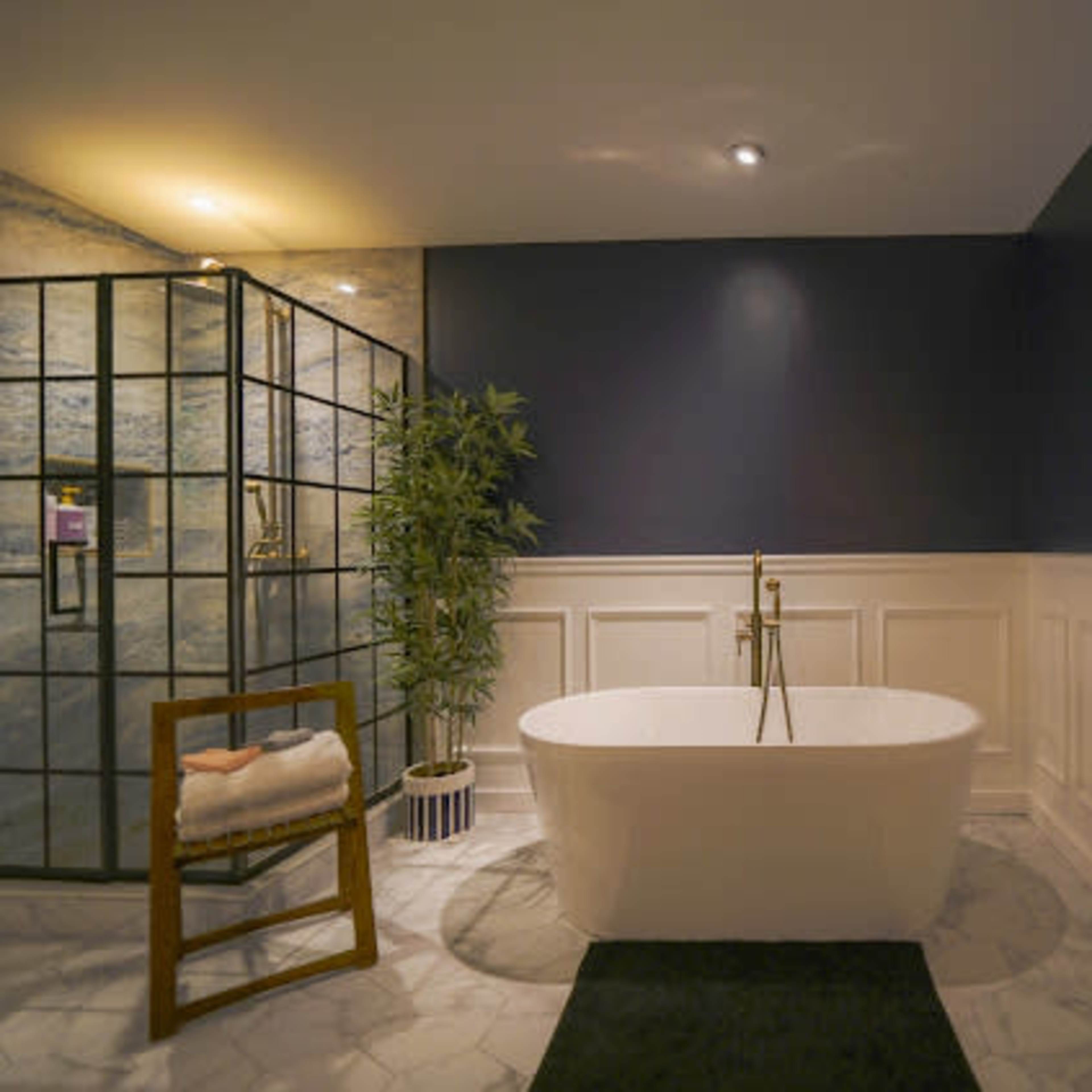 A modern bathroom featuring a freestanding white bathtub, a glass shower enclosure, and a decorative plant beside a wooden chair.