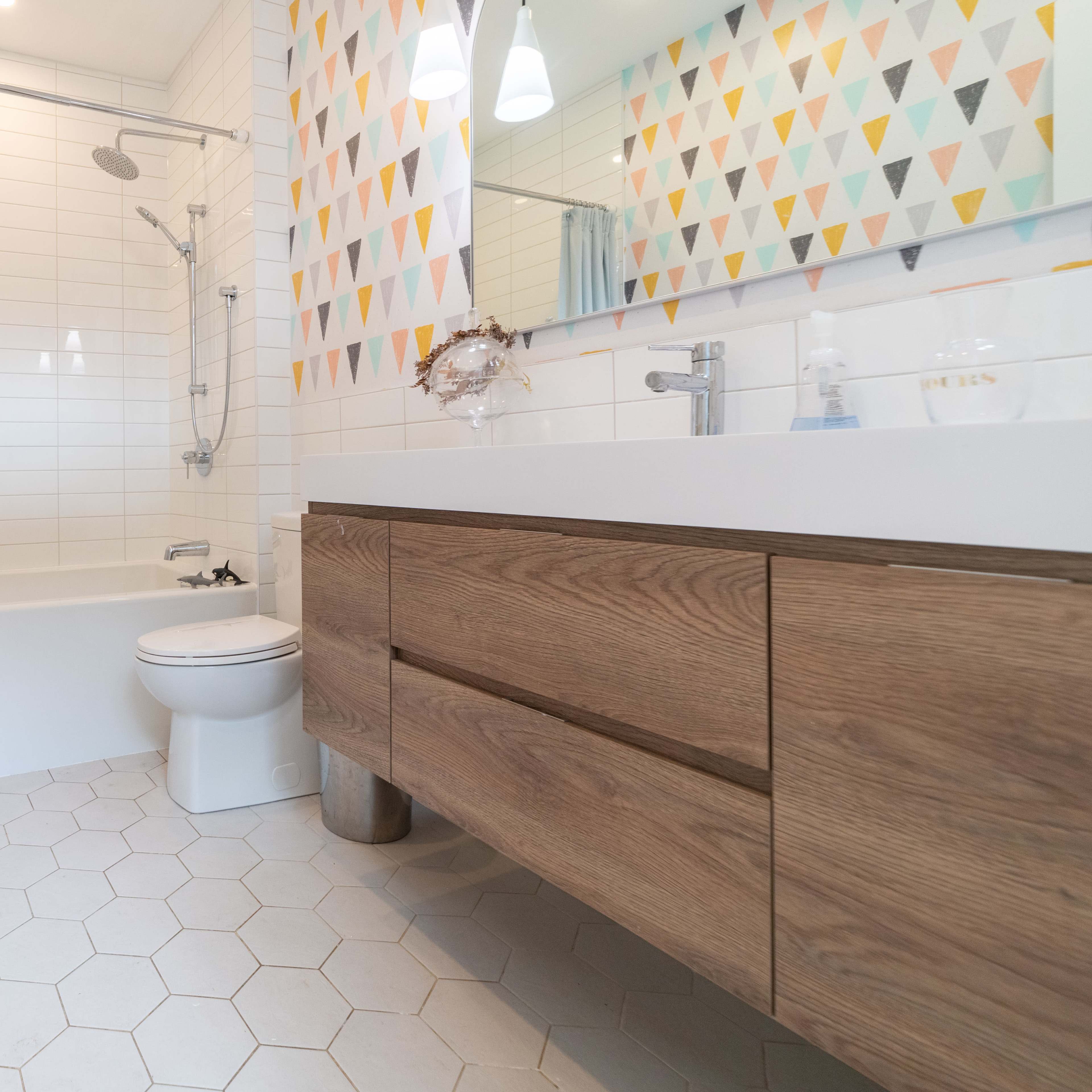 A modern bathroom featuring a wooden vanity, a white bathtub, and colorful triangular wall patterns.