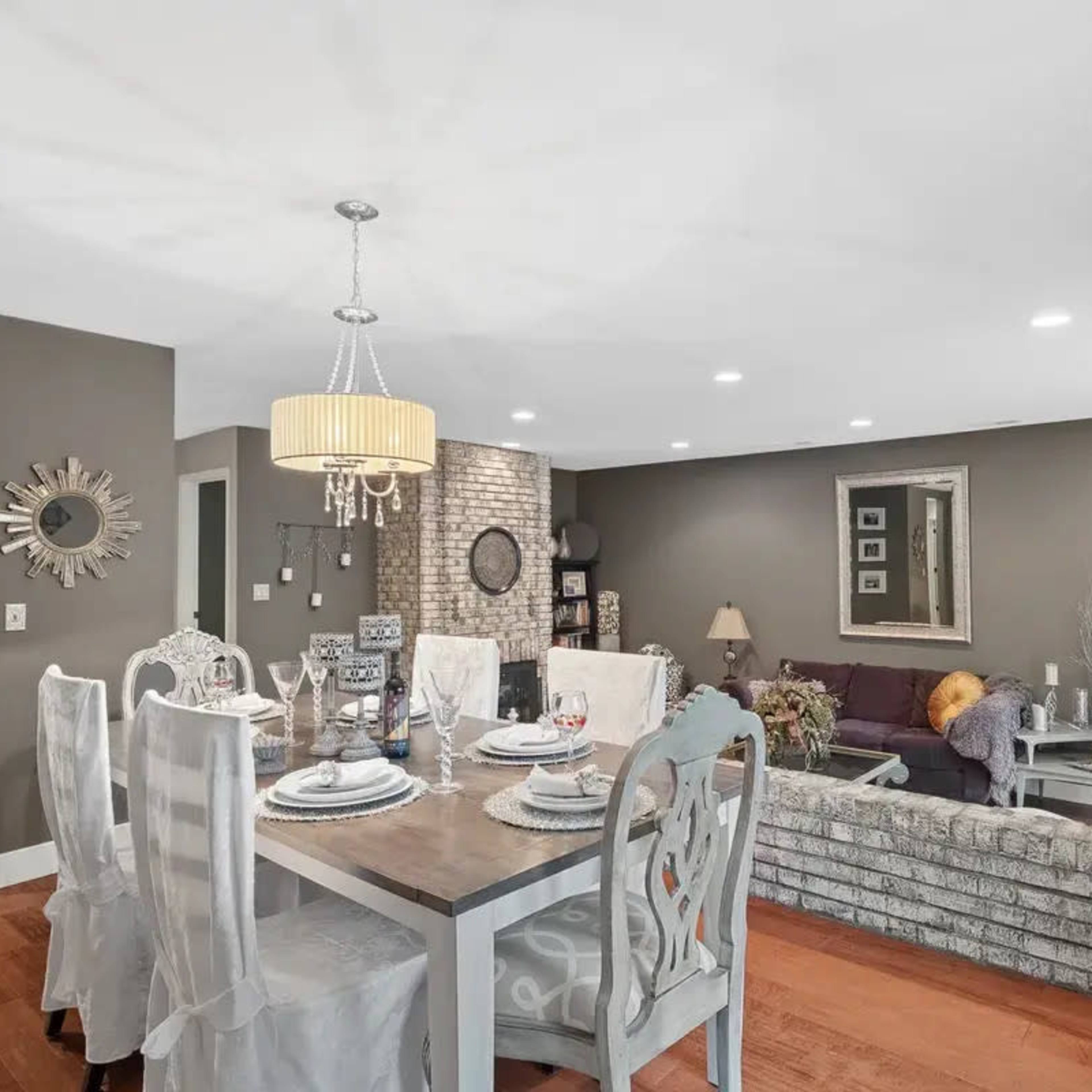 A dining area with a table set for a meal is adjacent to a living room featuring a sofa and decorative elements against a neutral-colored wall.