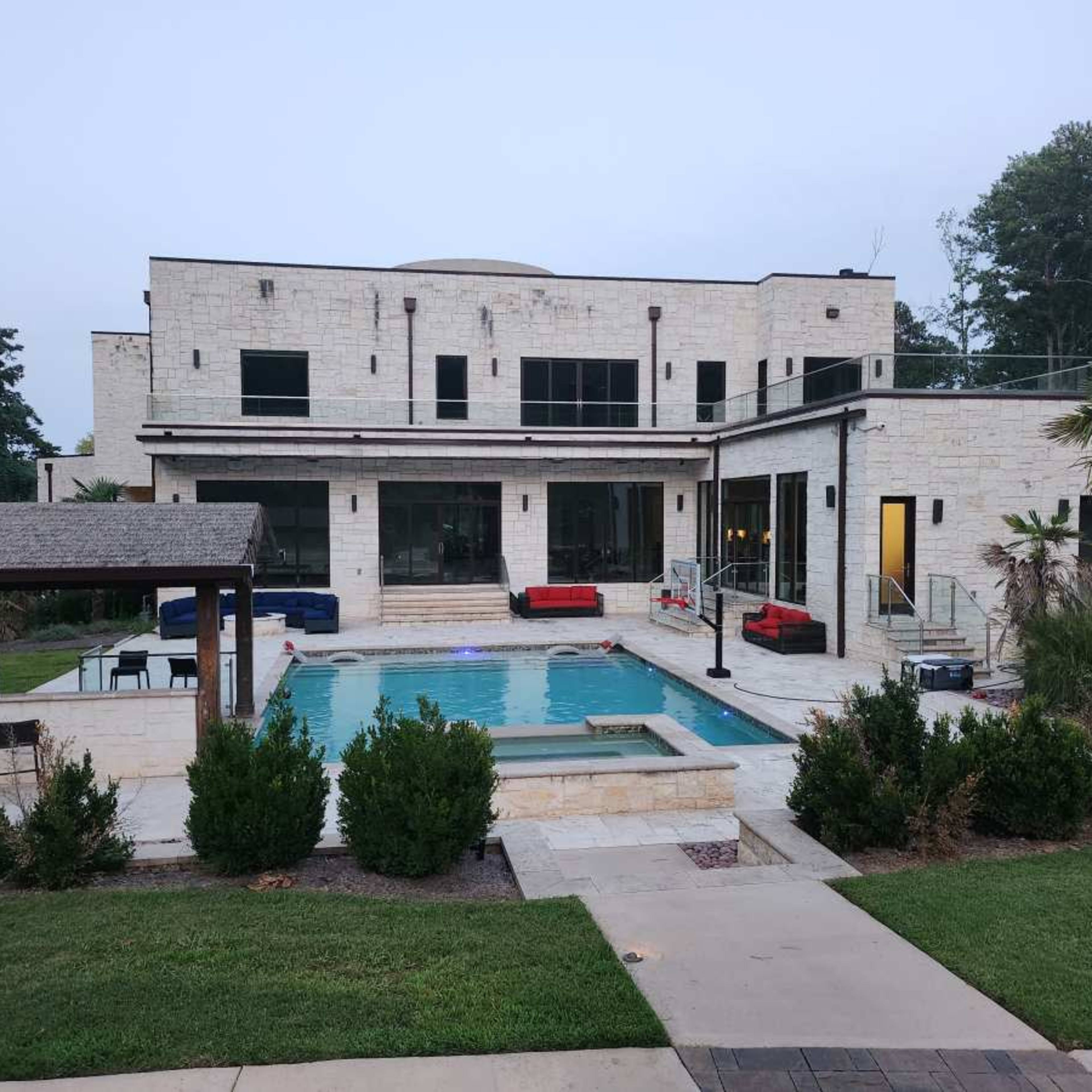 A modern two-story house with large windows and a swimming pool surrounded by landscaped gardens and outdoor seating.