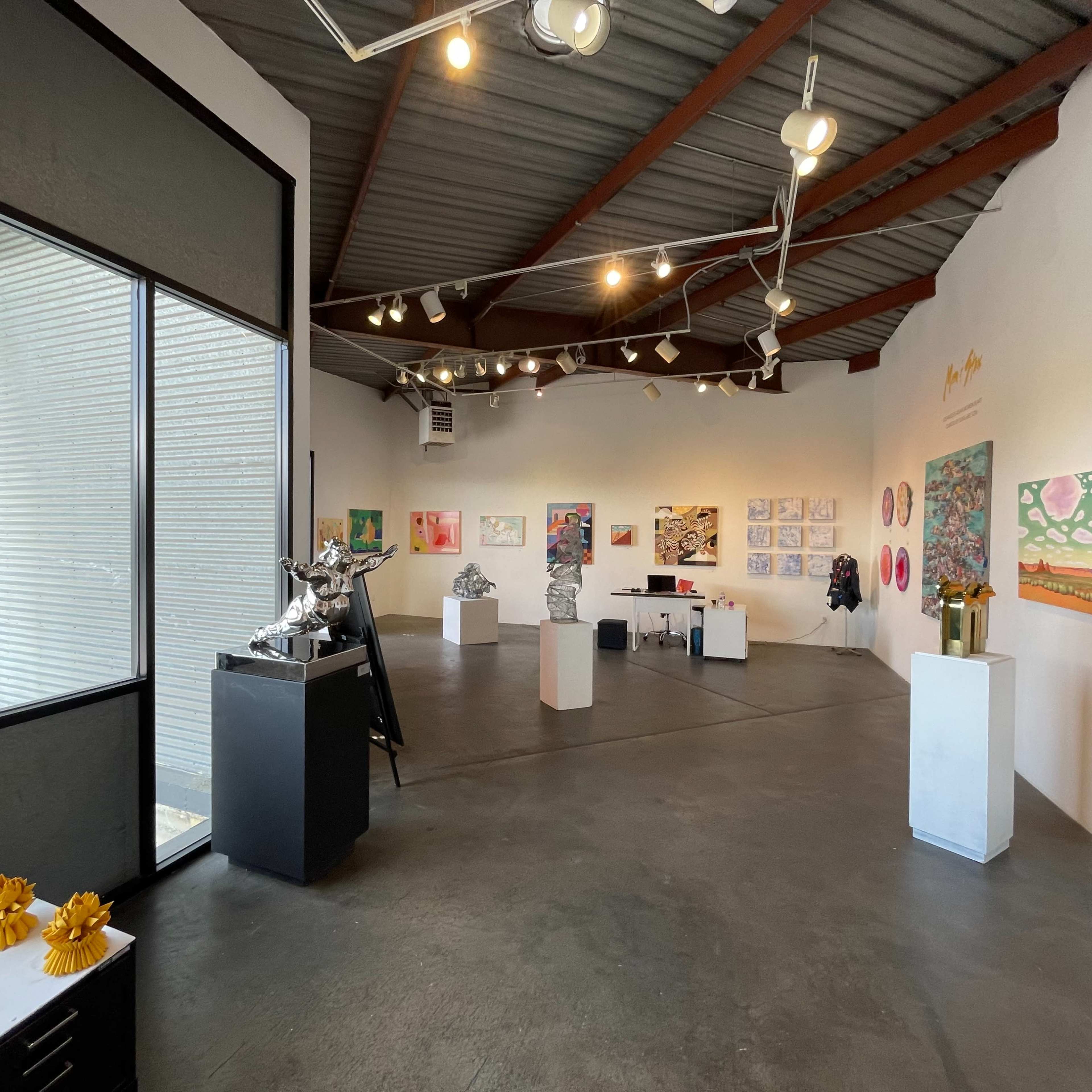 An art gallery interior with various artworks displayed on the walls and sculptures on pedestals throughout the space.