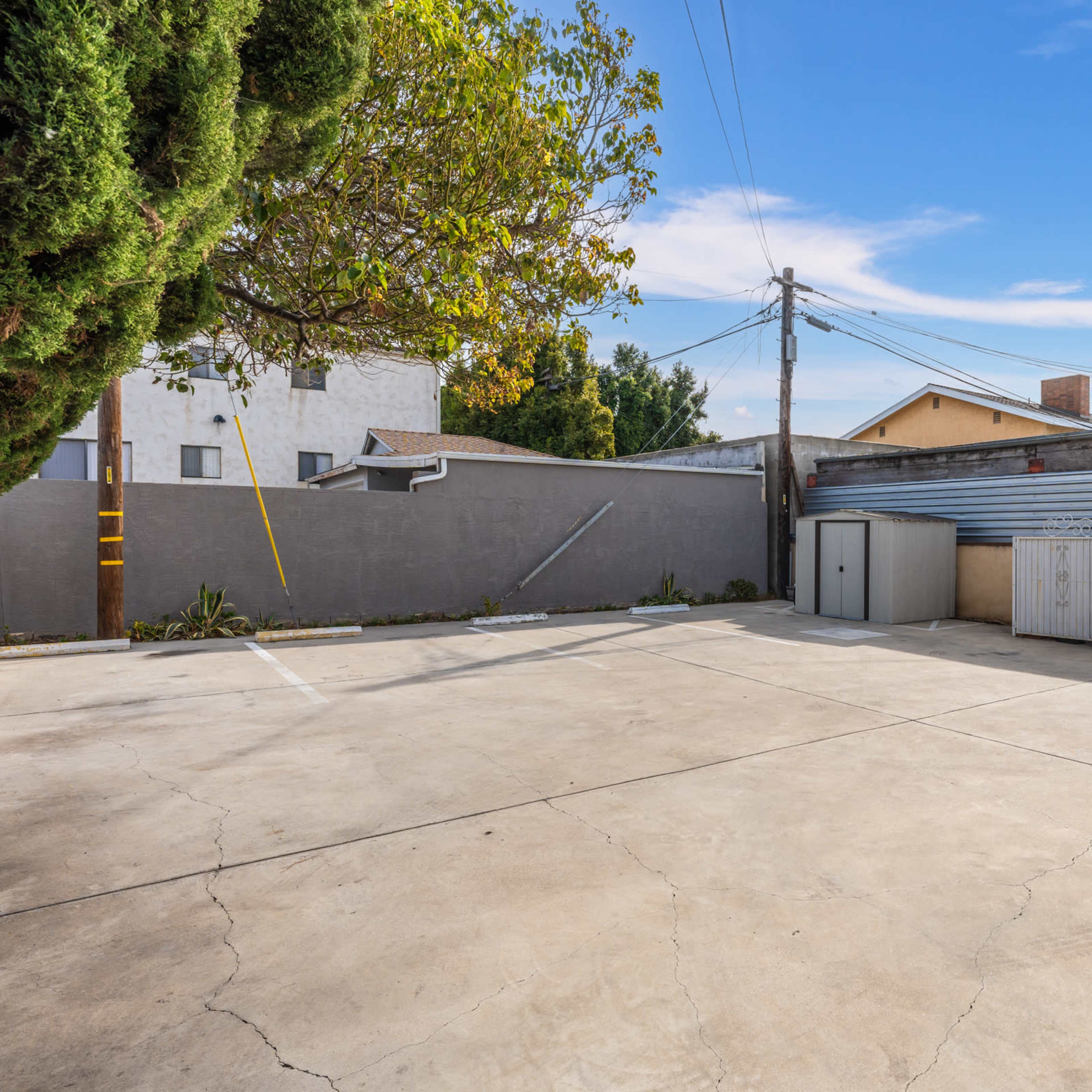 A concrete parking area enclosed by walls with utility poles and a storage shed in the background.