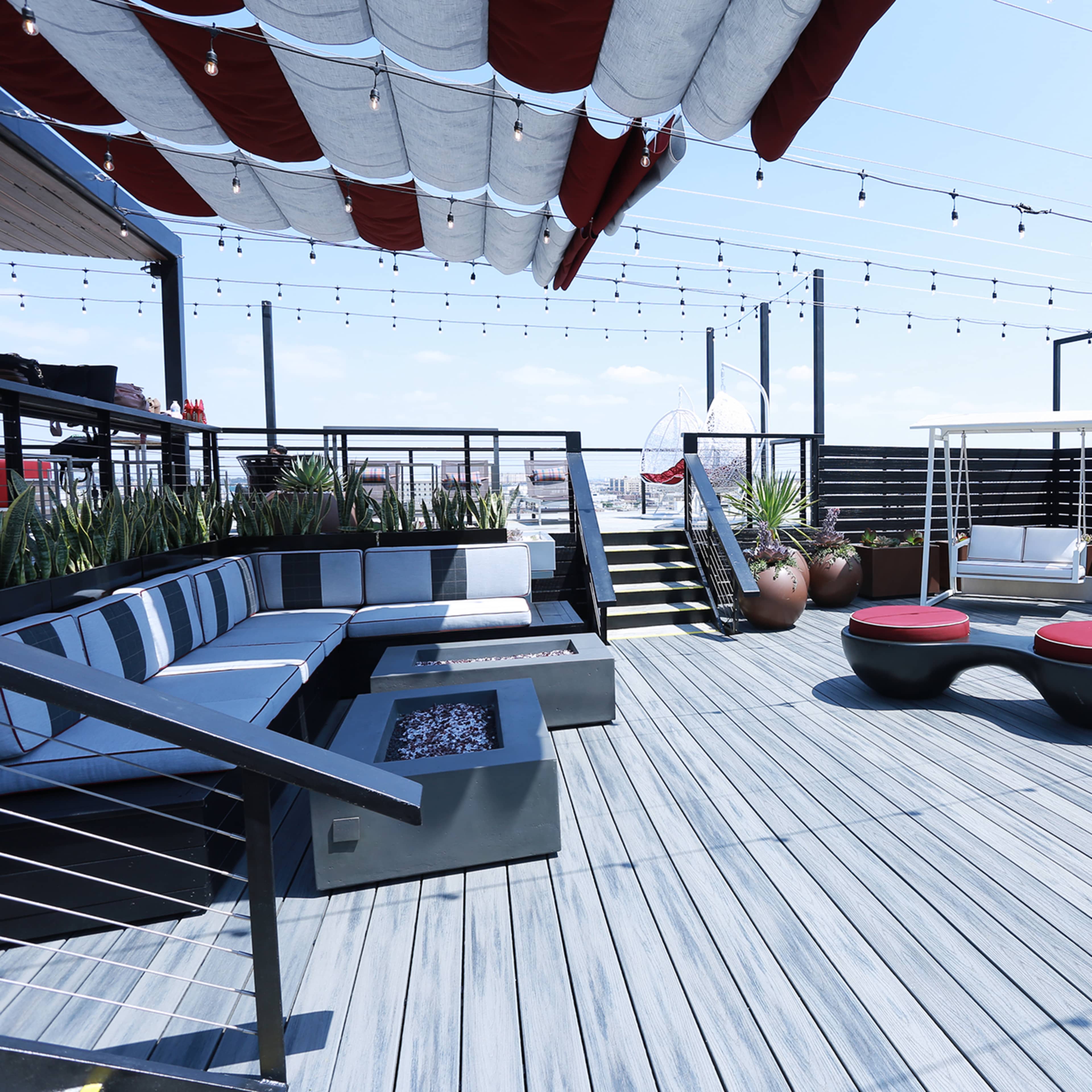A rooftop deck features modern seating arrangements, decorative plants, and string lights overhead.