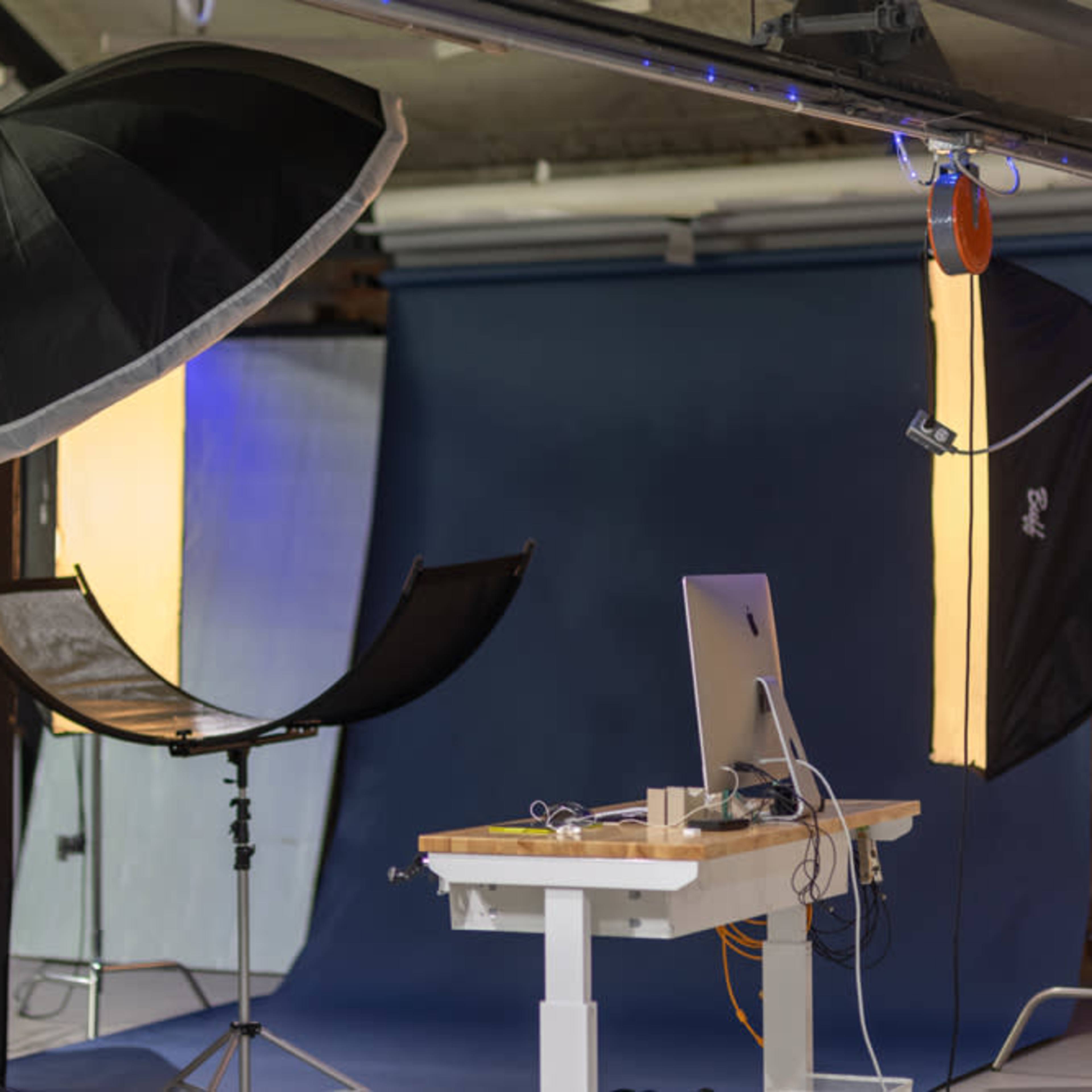 A photography studio setup with lighting equipment, a backdrop, and a computer on a table.