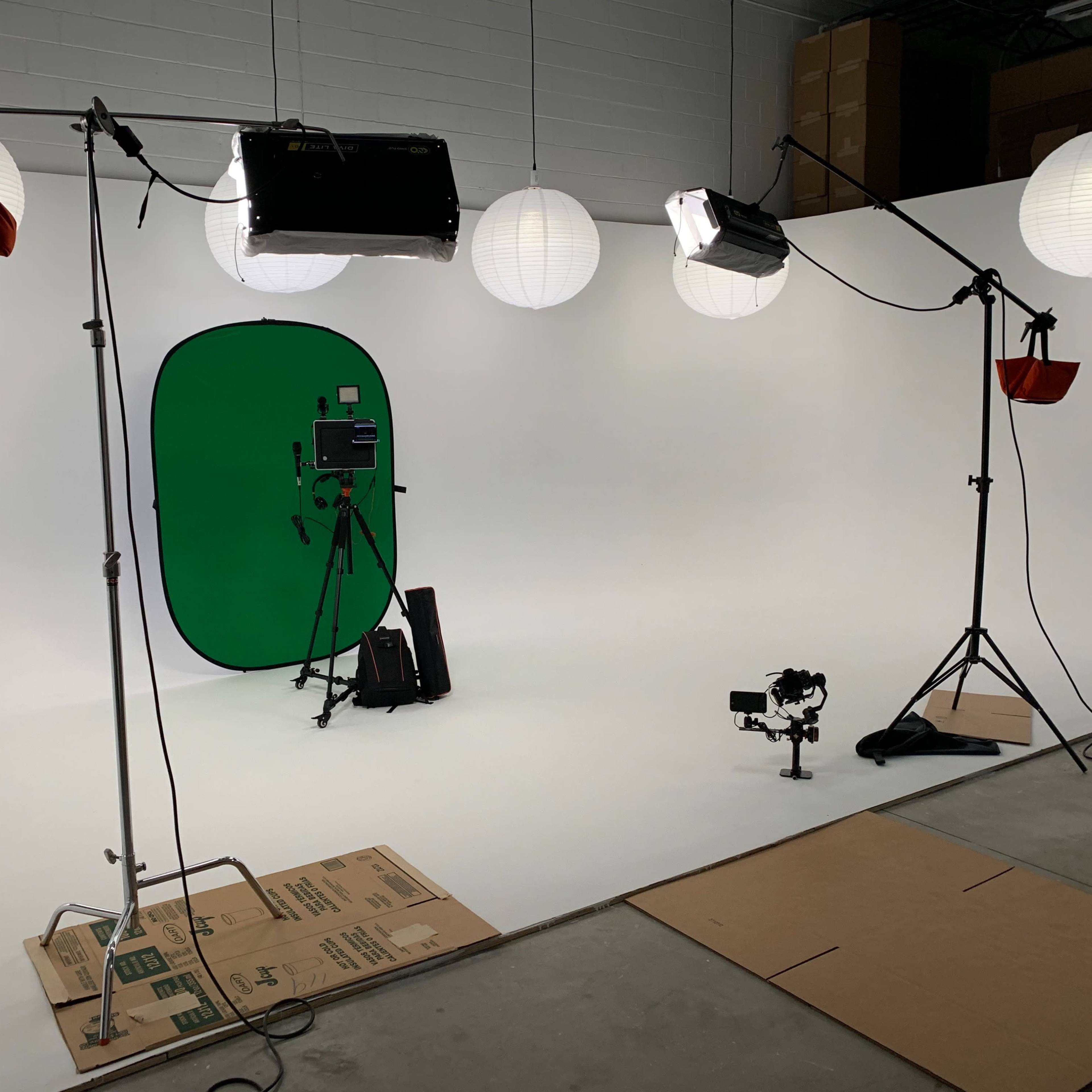 A photography studio setup with a green backdrop, lighting equipment, and a camera on a tripod.
