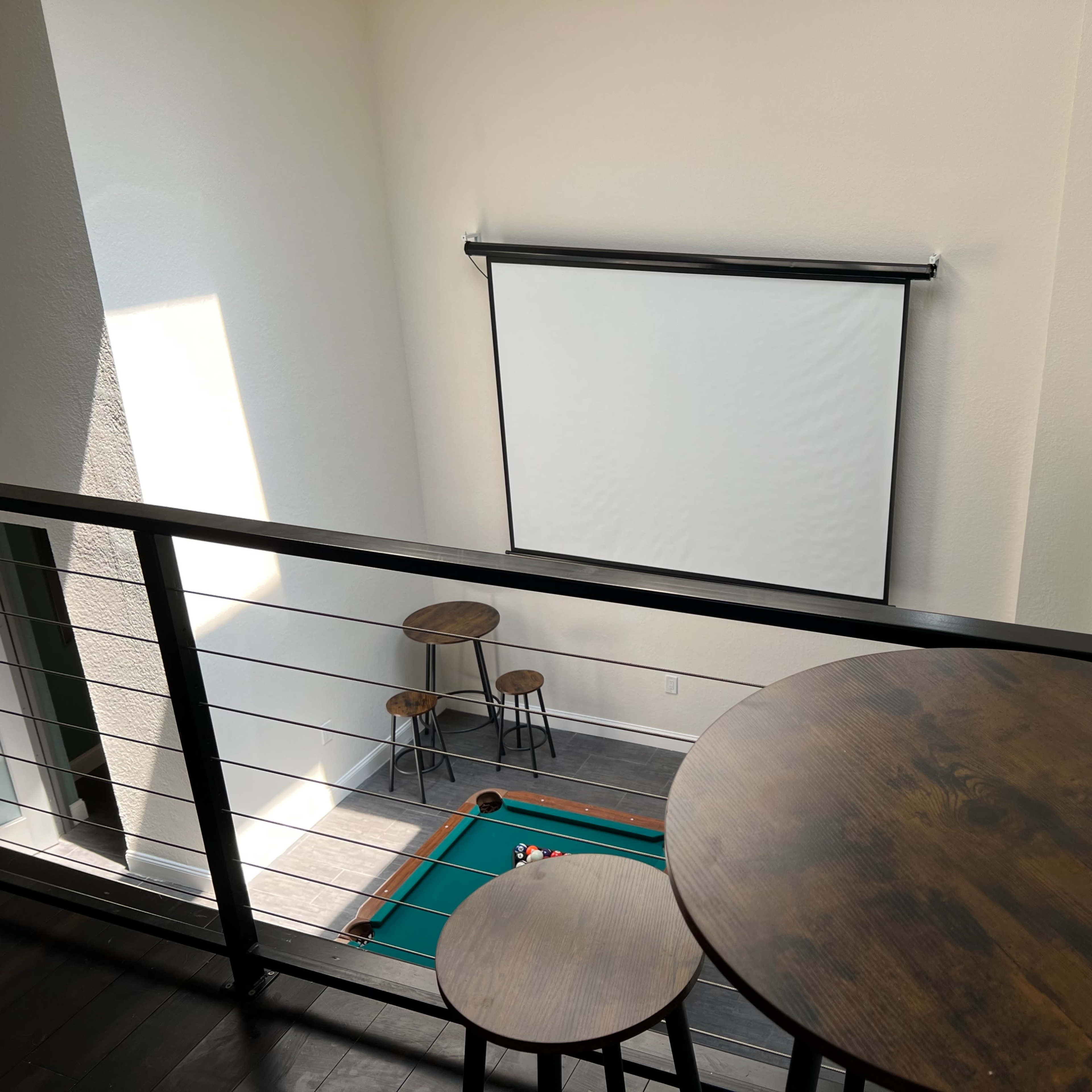 A second-floor view of a leisure area featuring a pool table, a projection screen, and two small round tables.