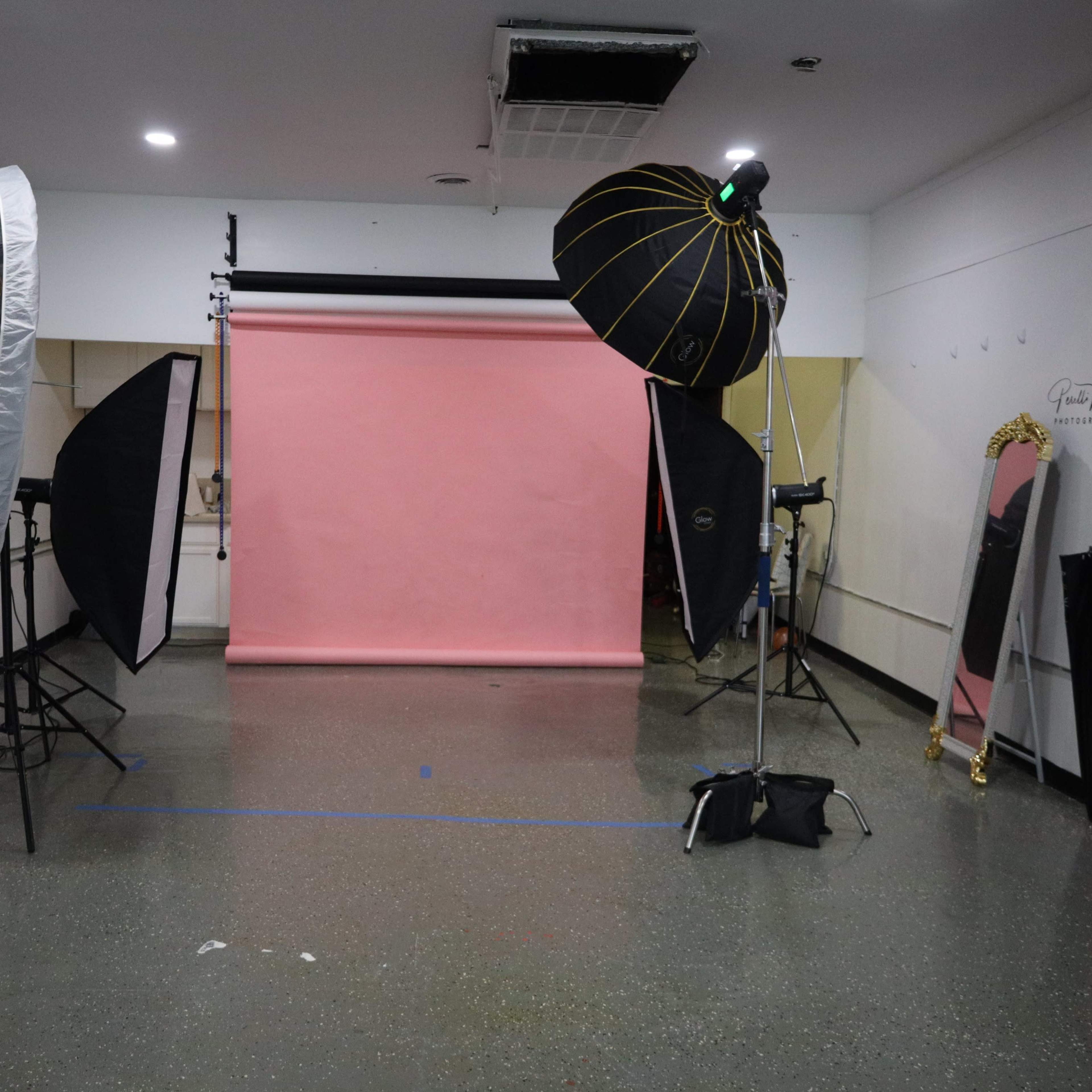 A photography studio is set up with softbox lights, a pink backdrop, and various studio equipment.