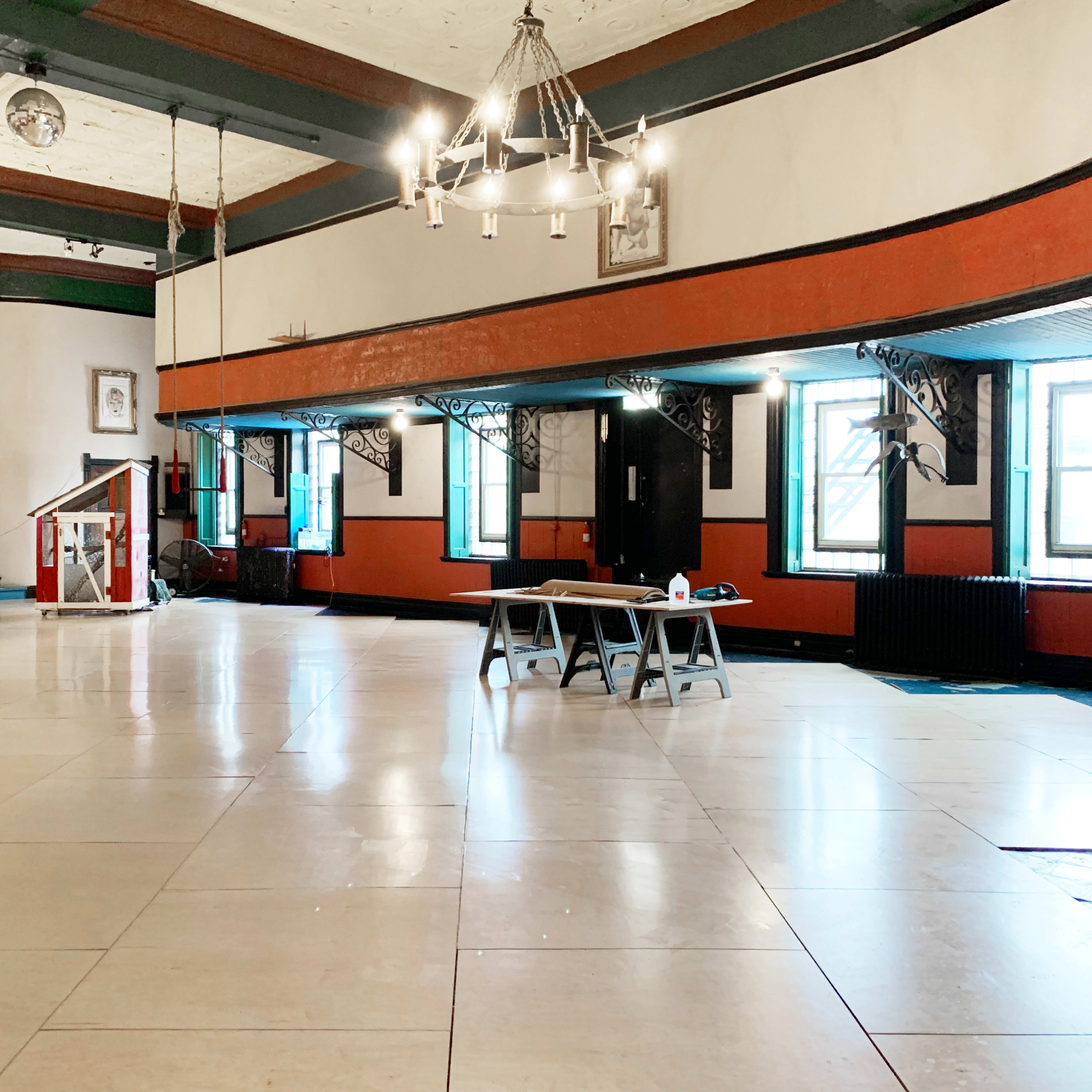 A spacious, empty room with a polished floor, large windows, and a raised platform at one end.