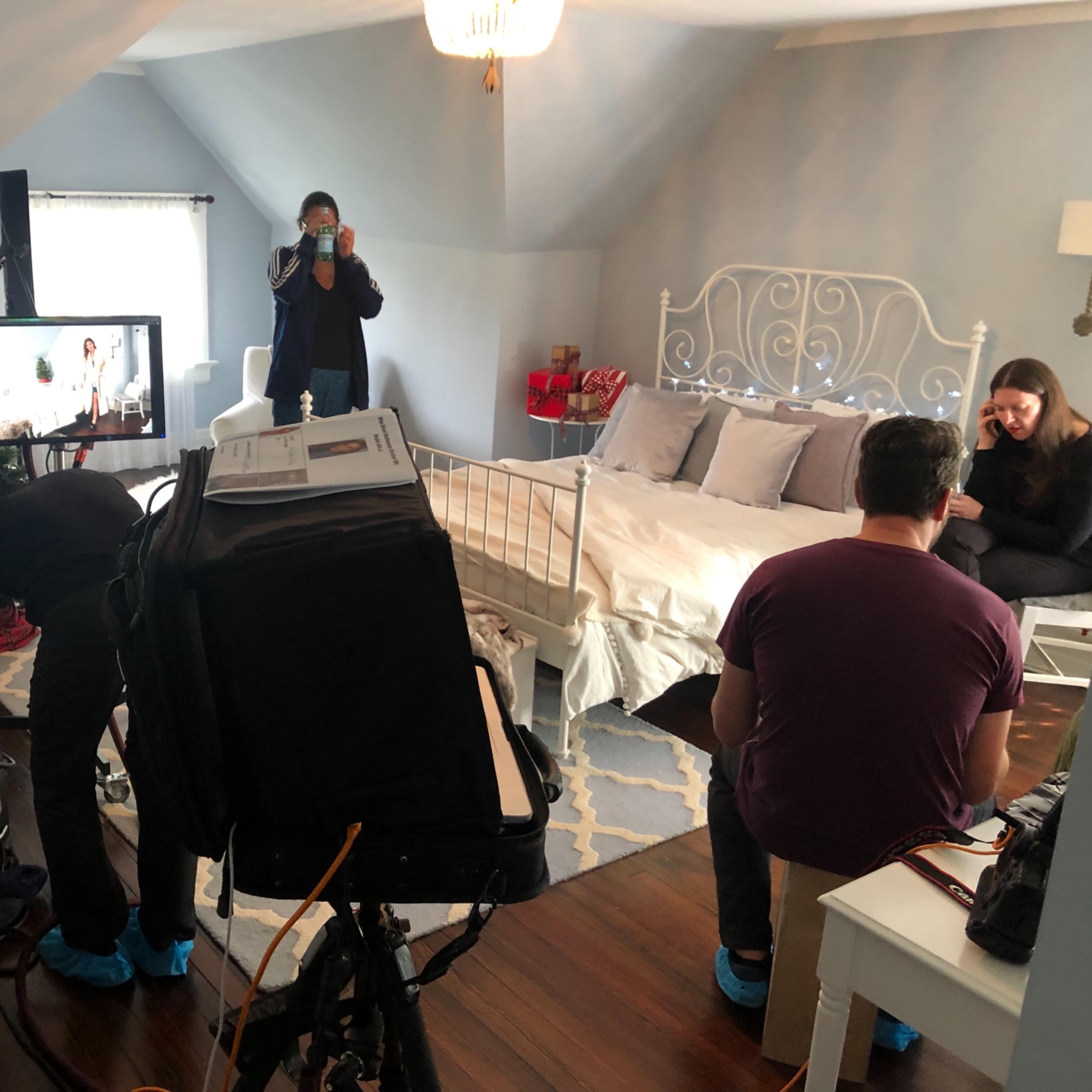 A film crew sets up equipment in a styled bedroom for a shooting scene.