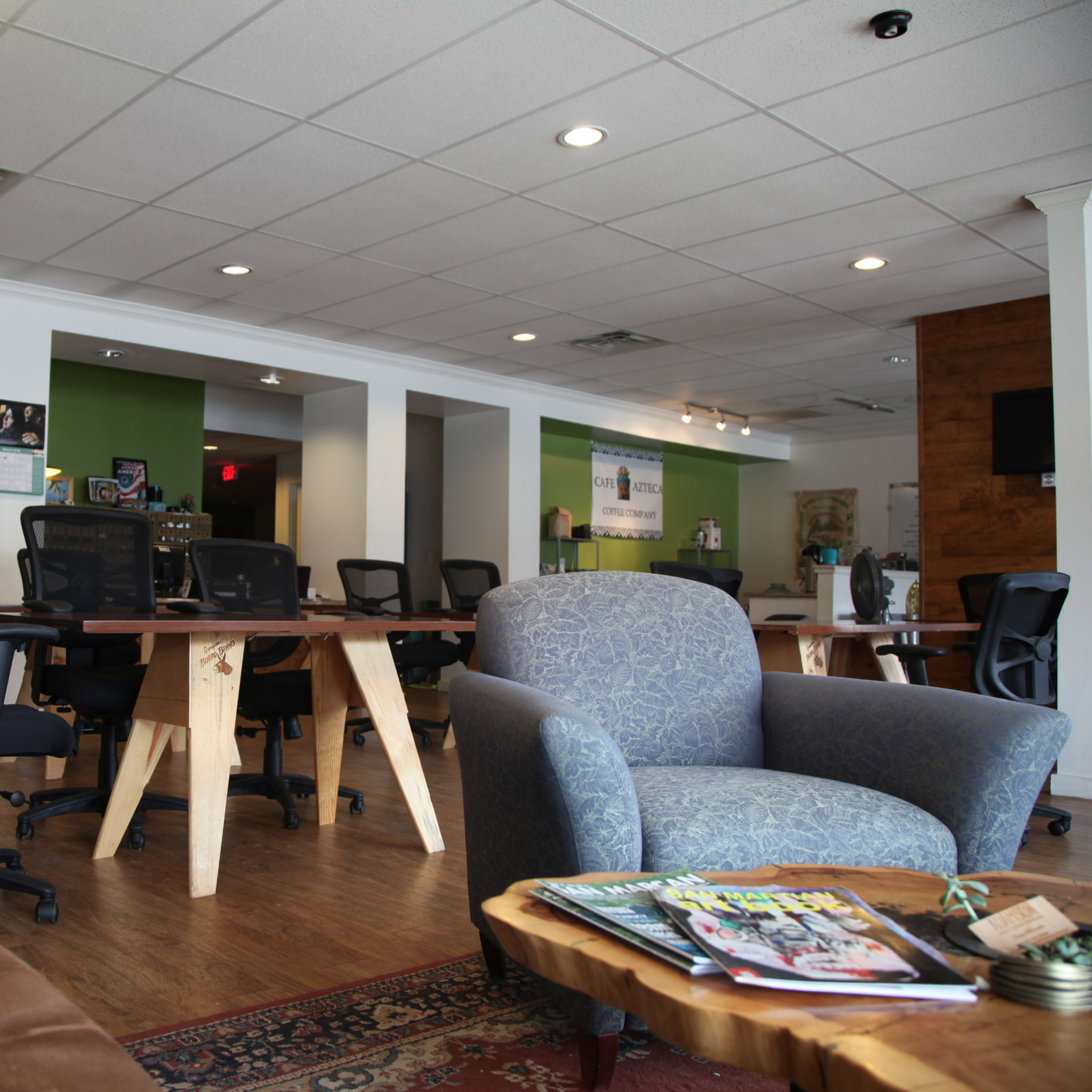 A modern office space with several desks and chairs, a cozy seating area, and green accent walls.