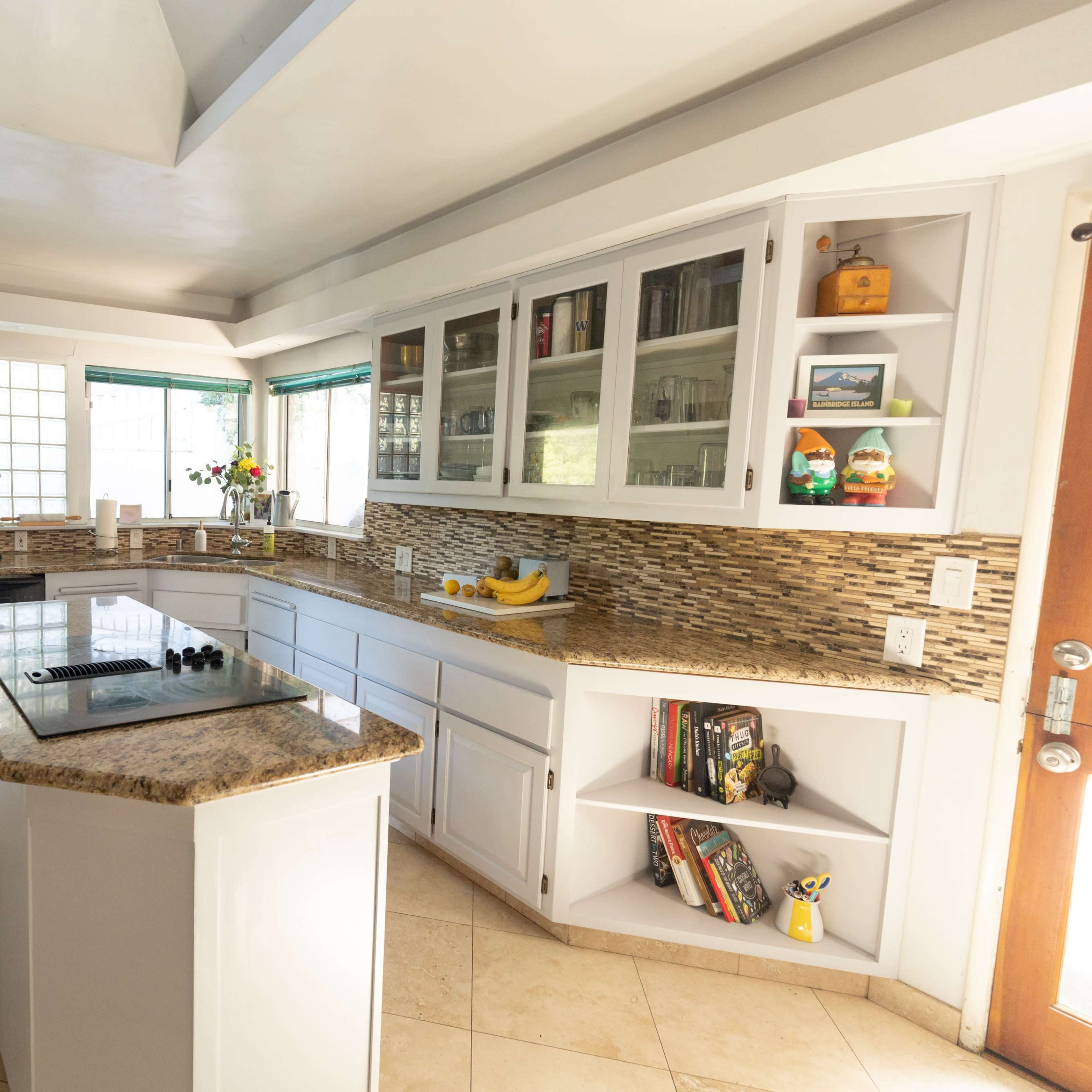 A modern kitchen with white cabinets, a granite countertop, and a tiled backsplash, featuring appliances and decorative items.