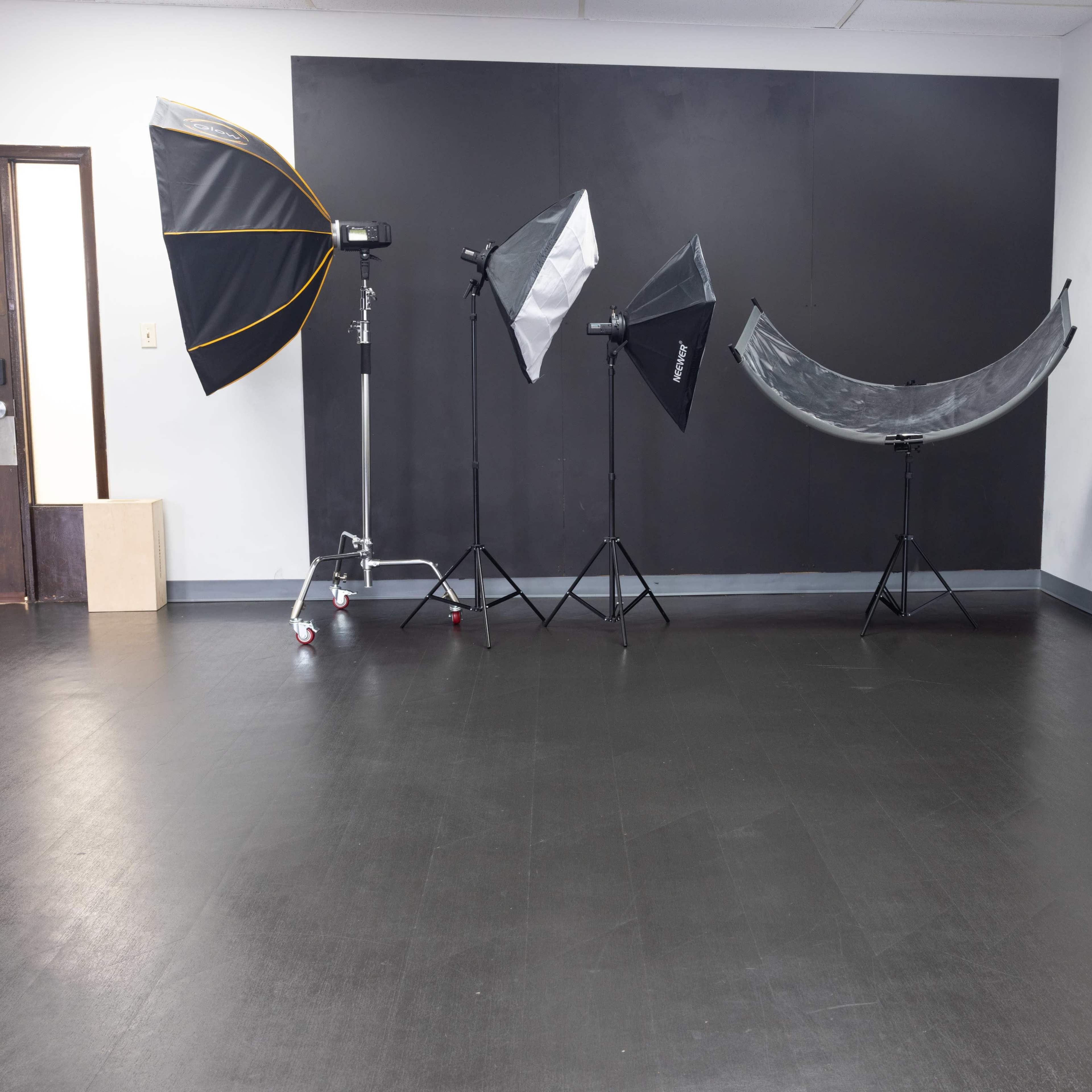 A photography studio with various lighting equipment, including umbrellas and softboxes, set against a dark backdrop.
