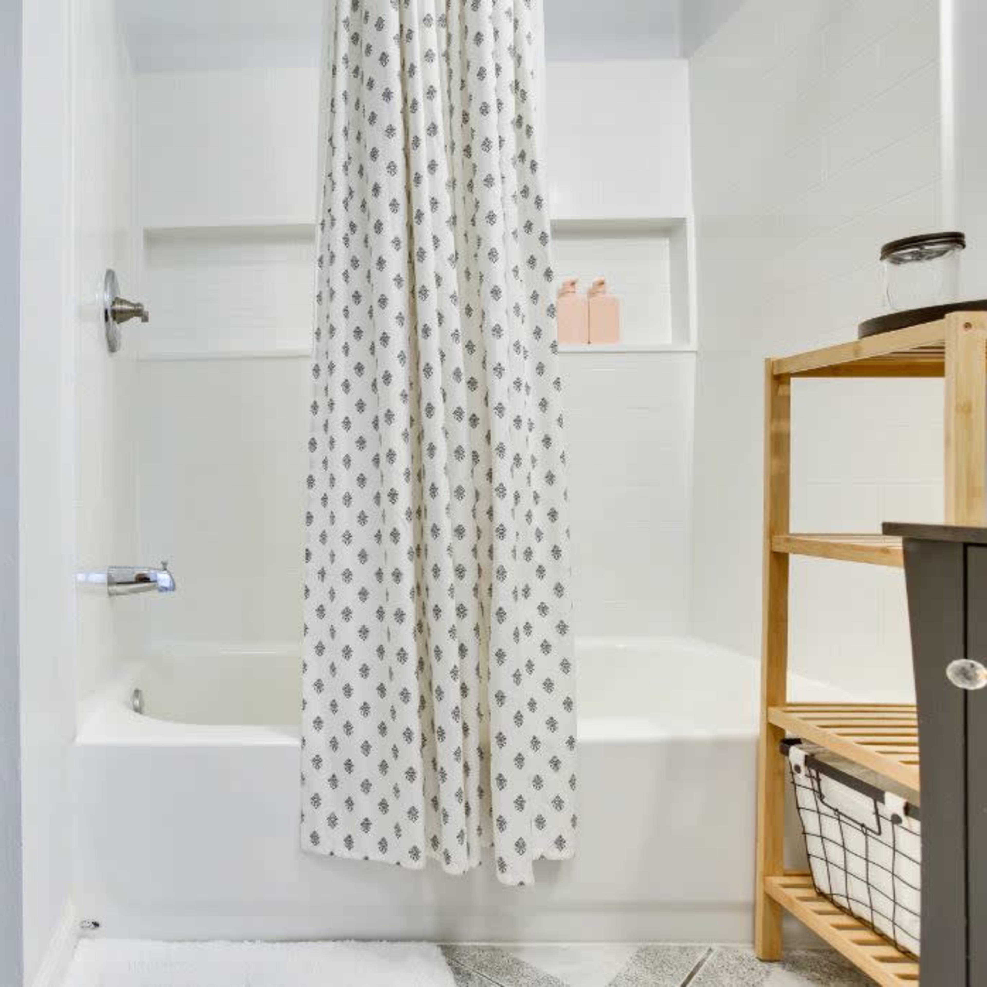 A clean bathroom features a bathtub with a shower curtain, a toilet, and wooden storage for toiletries.