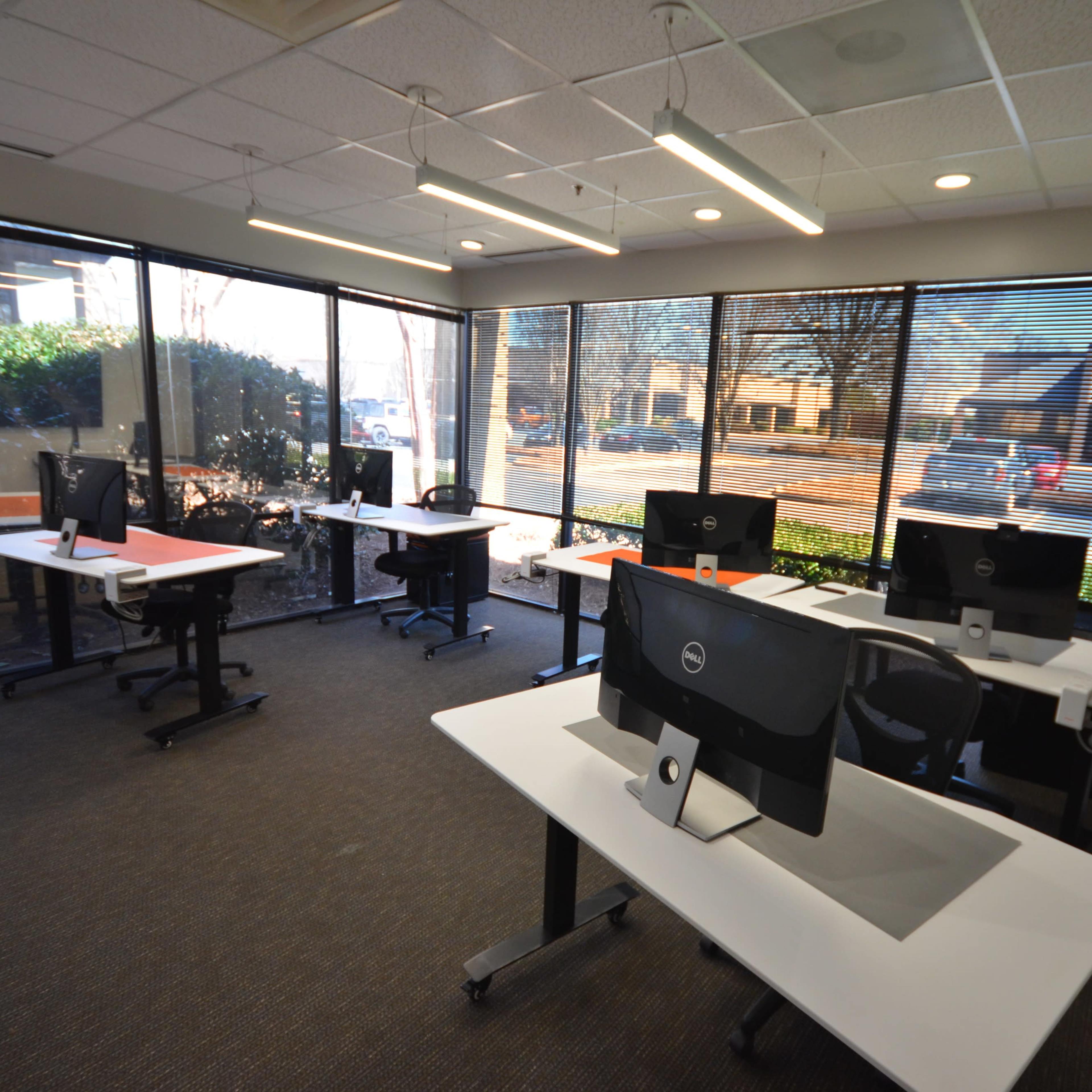 A modern office space with several desks equipped with computers and large windows allowing natural light to fill the room.