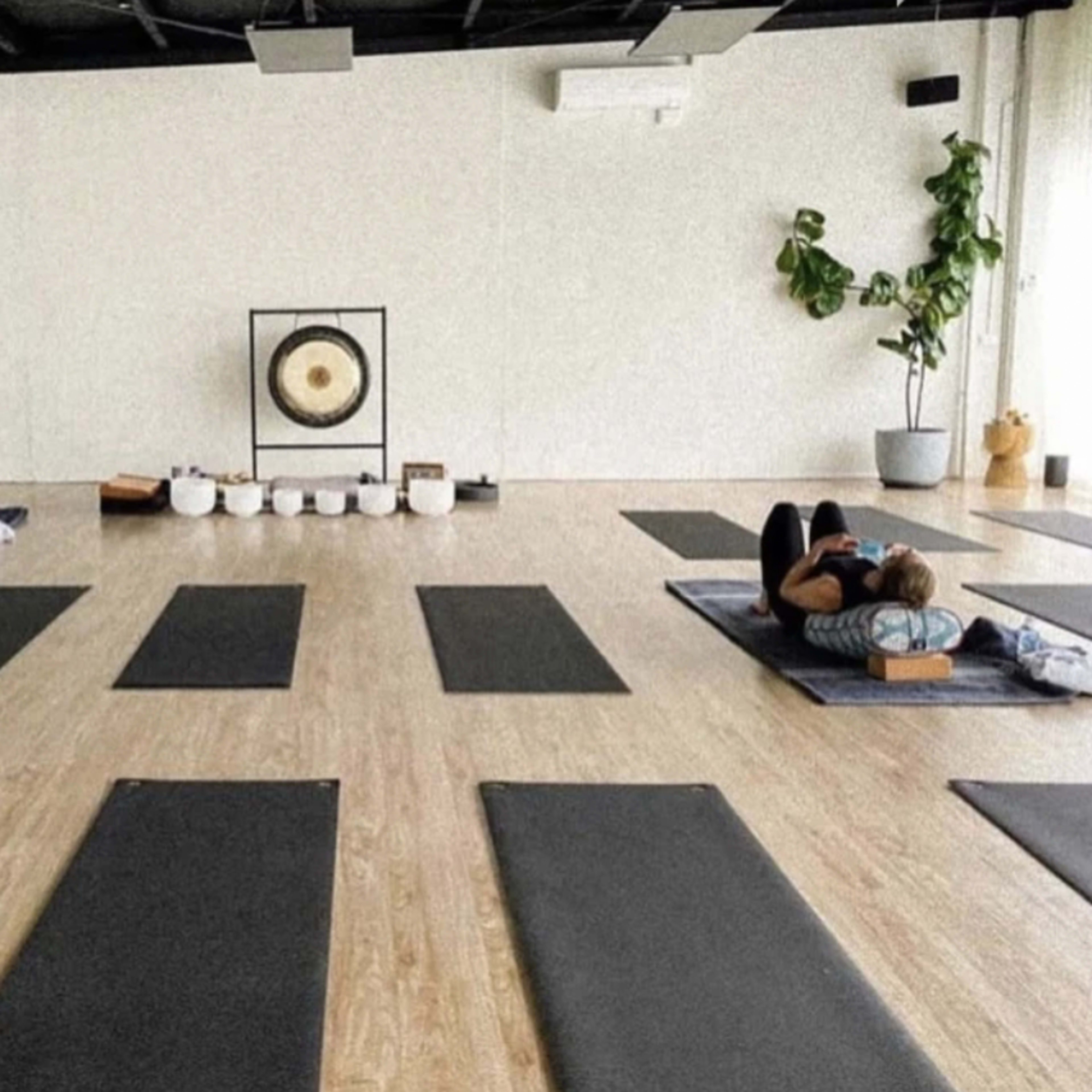 A spacious yoga studio with several exercise mats arranged on the floor, along with a gong and bowls displayed at the front.