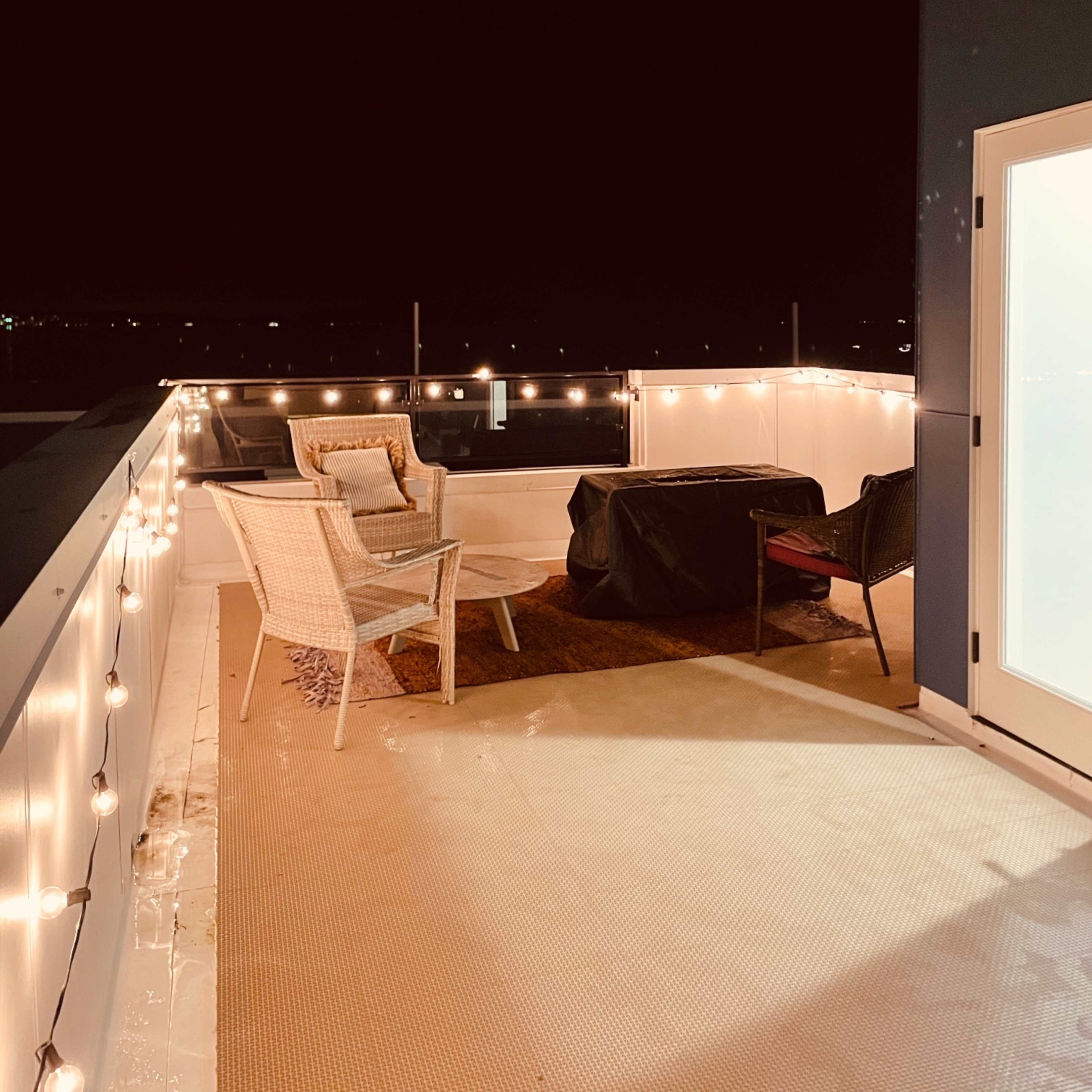 A rooftop terrace at night with string lights illuminating two chairs and a table.