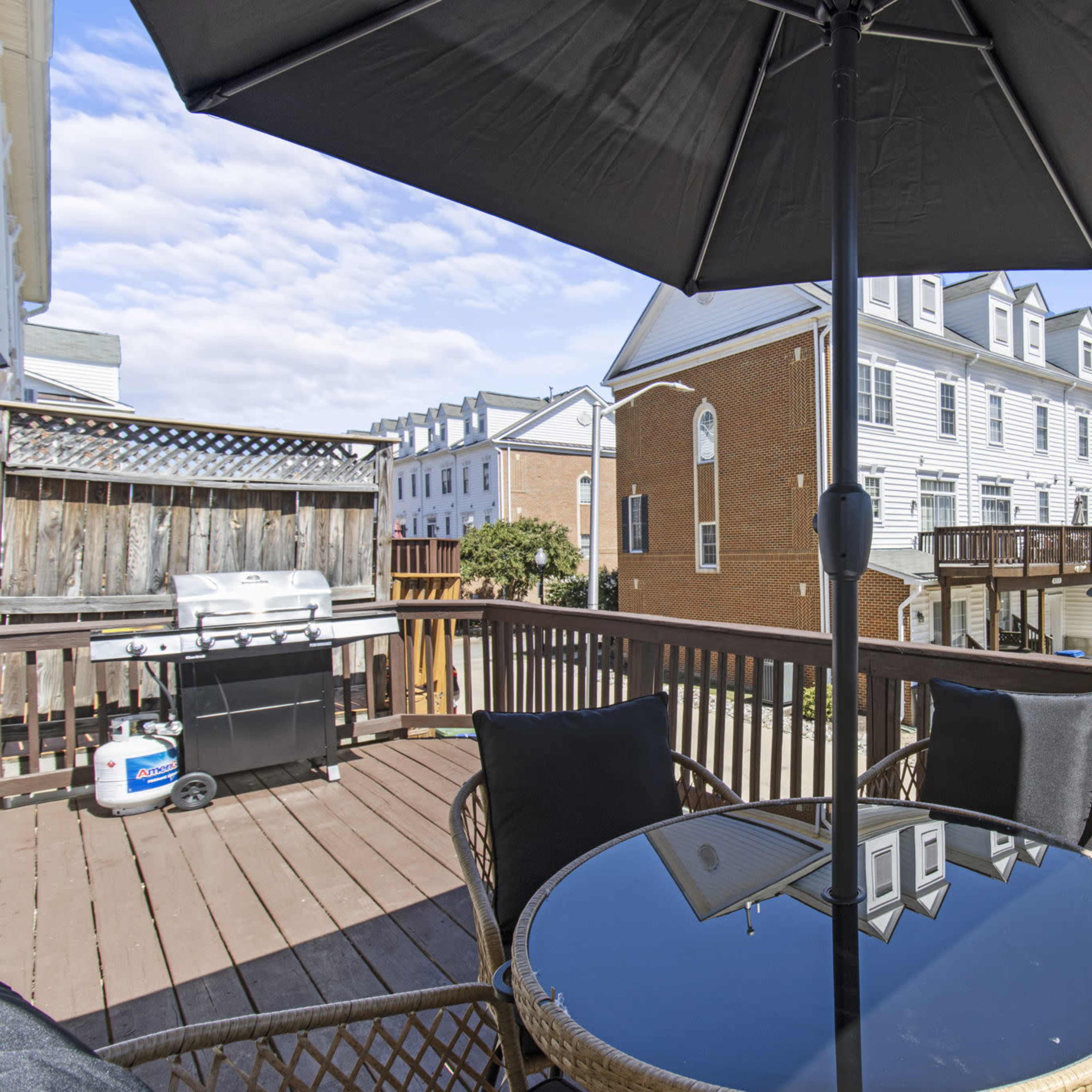 A patio with a black umbrella and a round table overlooks a row of townhouses and parked cars along a street.