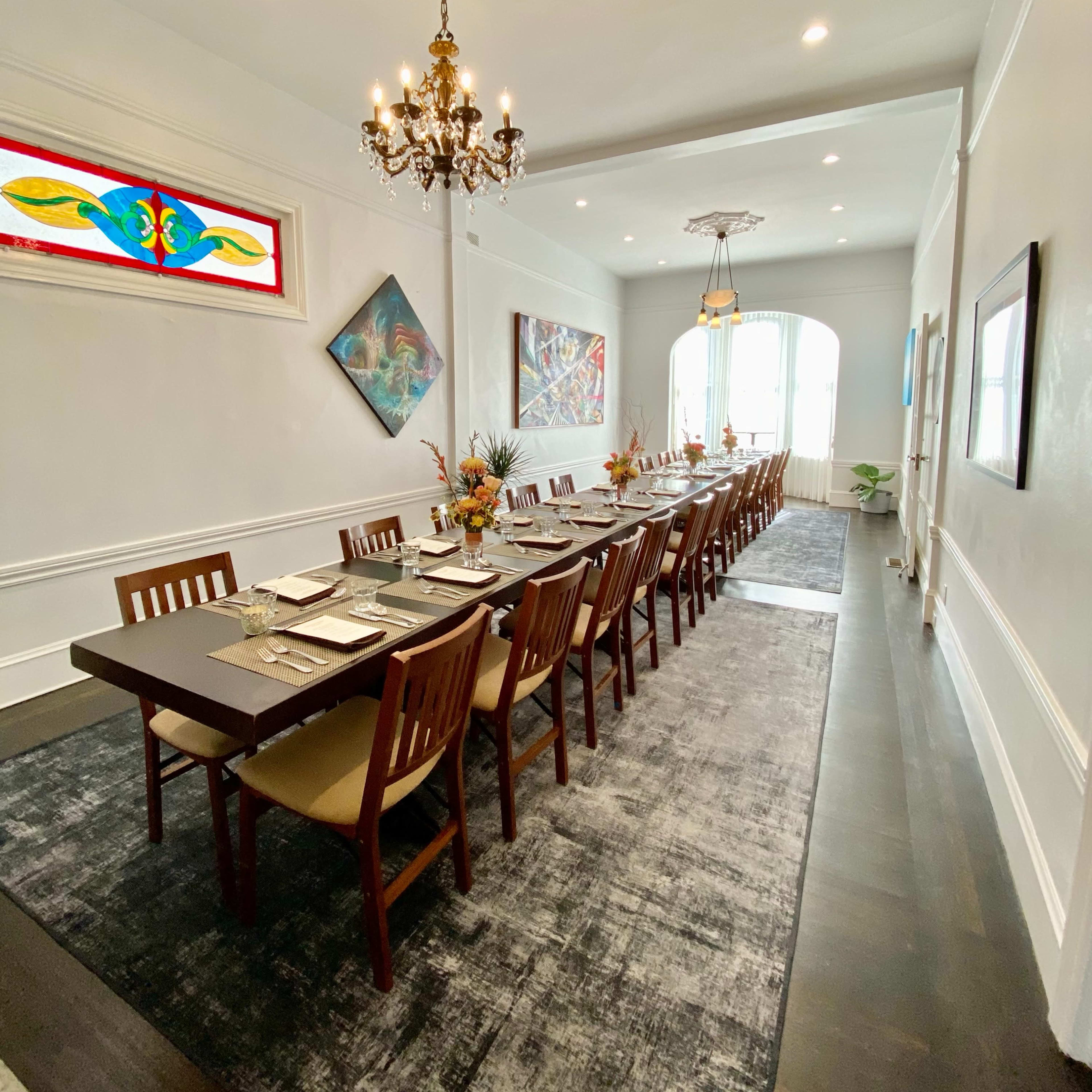 A long dining table is set in an elegantly decorated room with artistic wall pieces and a chandelier overhead.