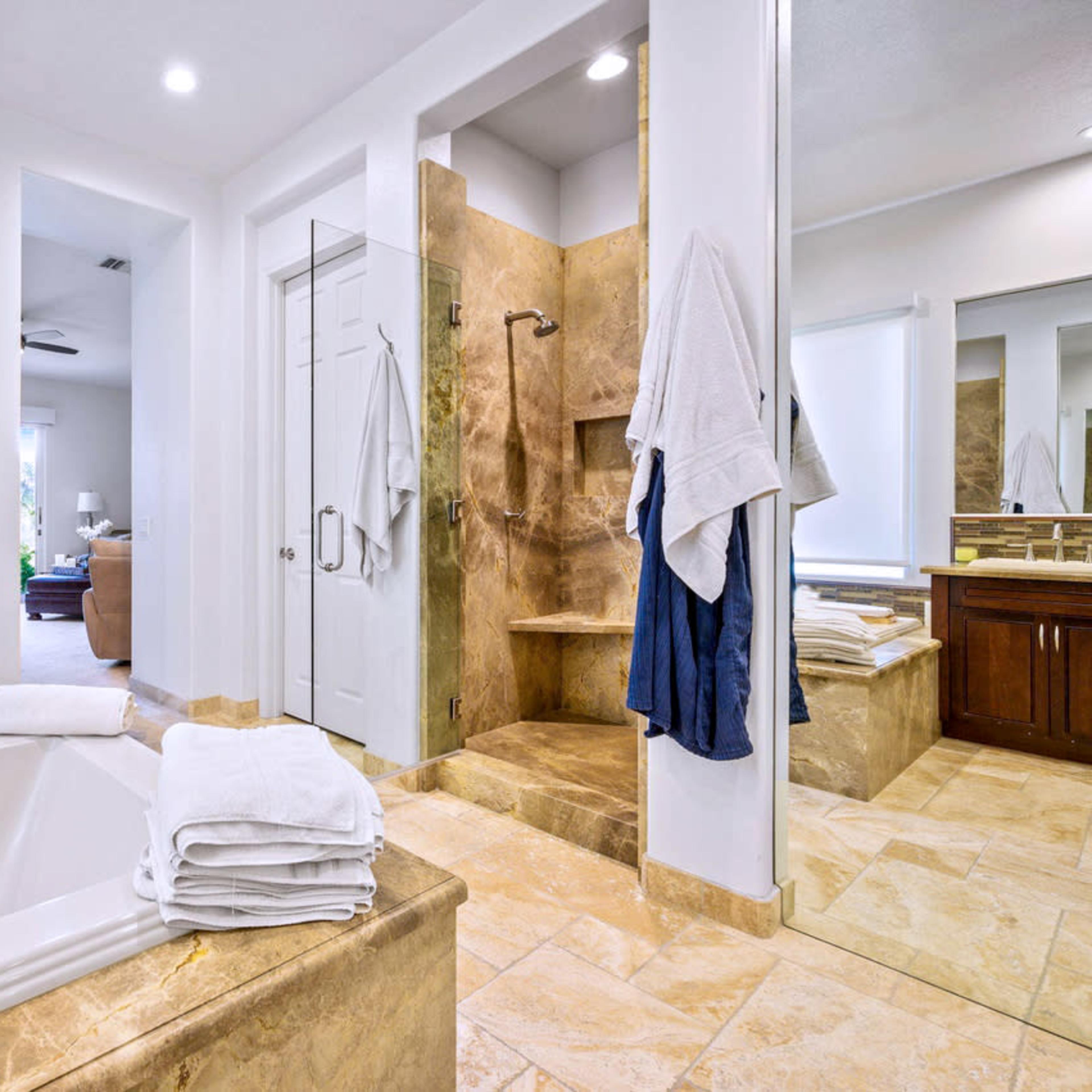 A modern bathroom featuring a freestanding bathtub, a walk-in shower, dual sinks with wooden cabinets, and large mirrors.