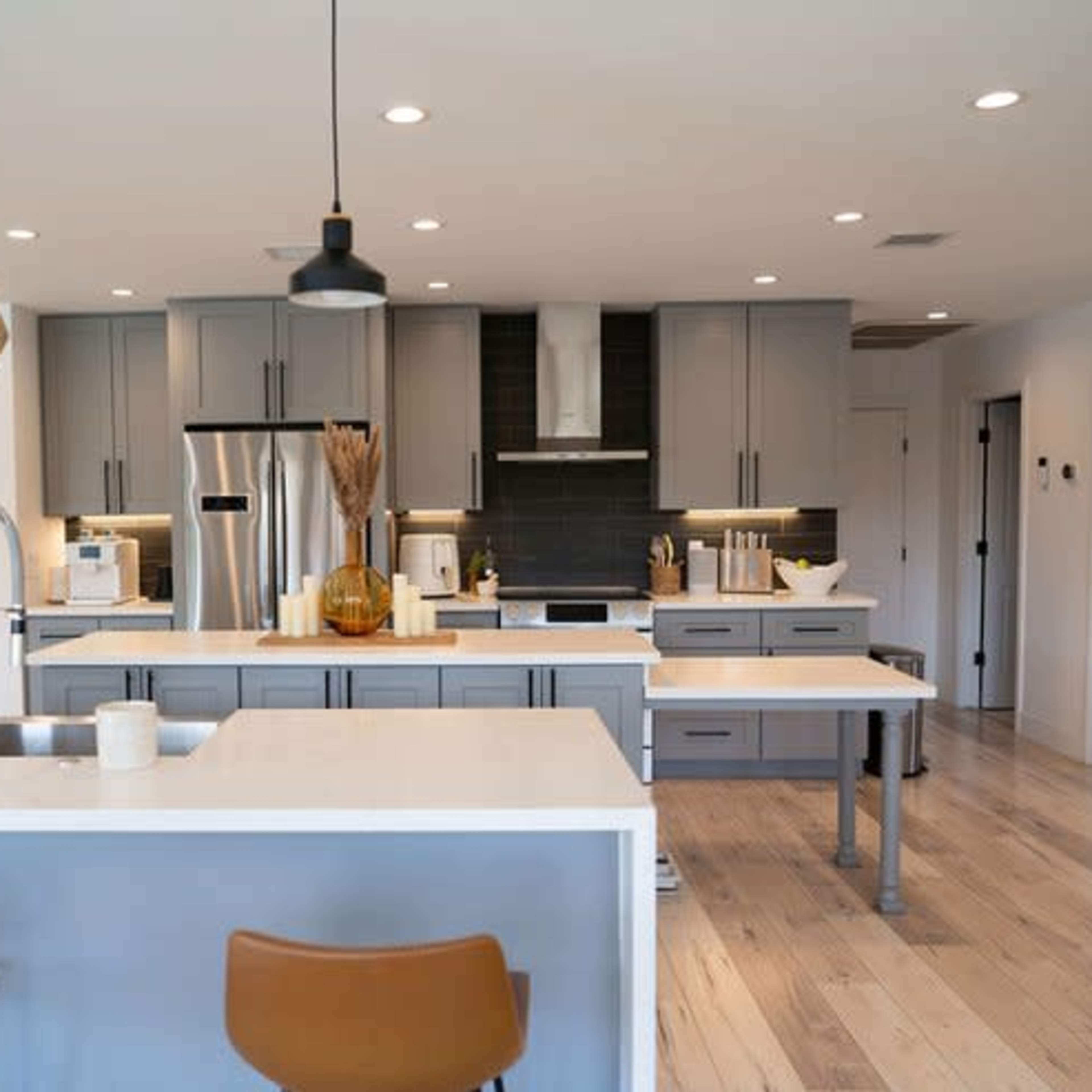 A modern kitchen with gray cabinets, stainless steel appliances, a large island with bar seating, and wood flooring.