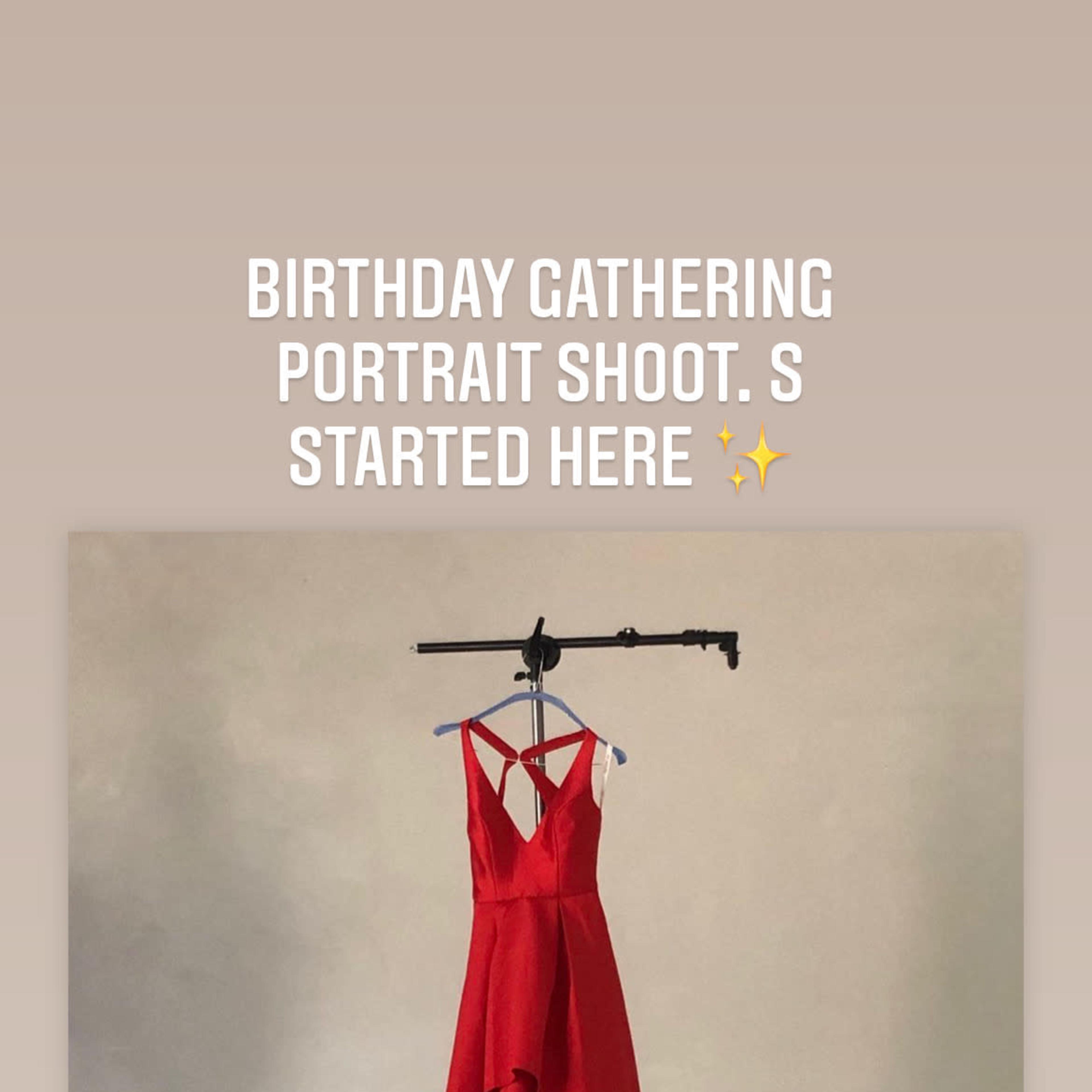 A red dress is hung on a clothing rack against a plain backdrop in a portrait studio setting.