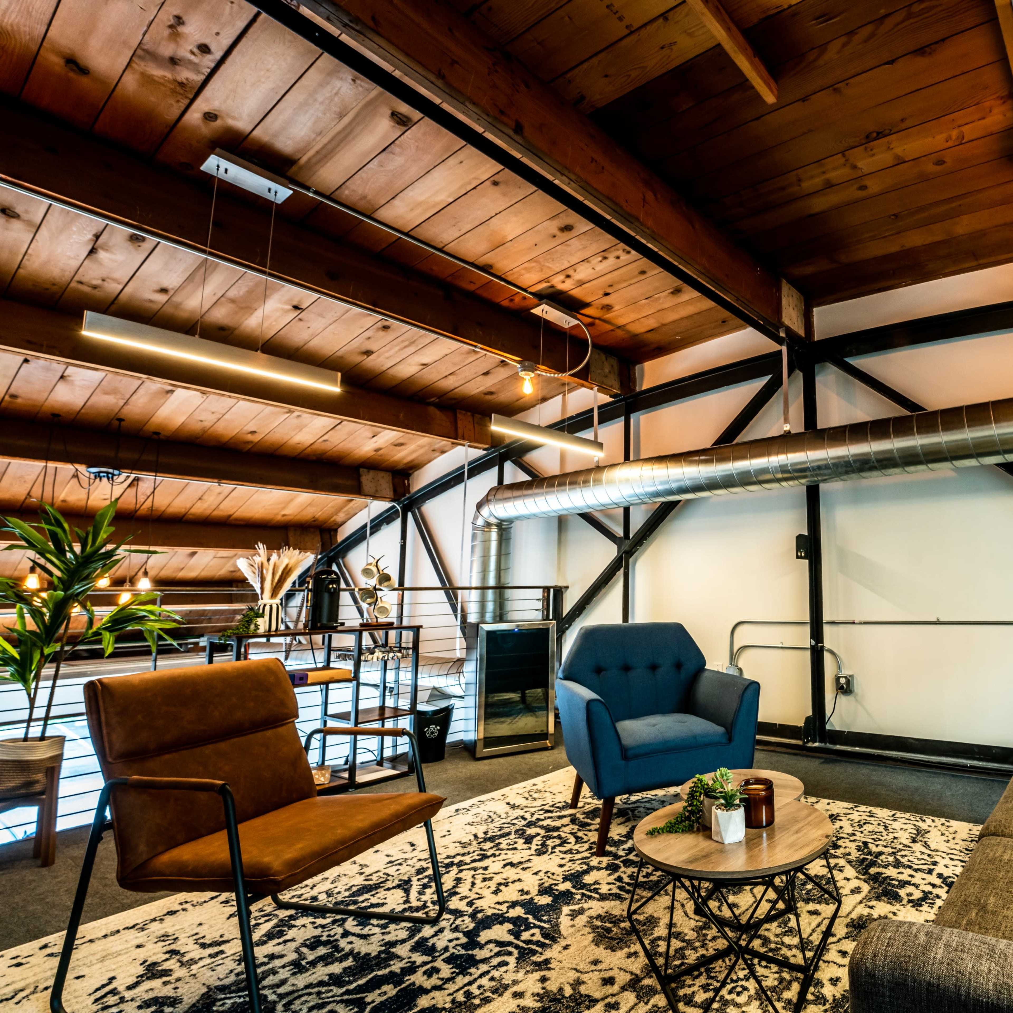 A modern living space with a wooden ceiling, a gray sofa, a blue armchair, and a small coffee table on a patterned rug.