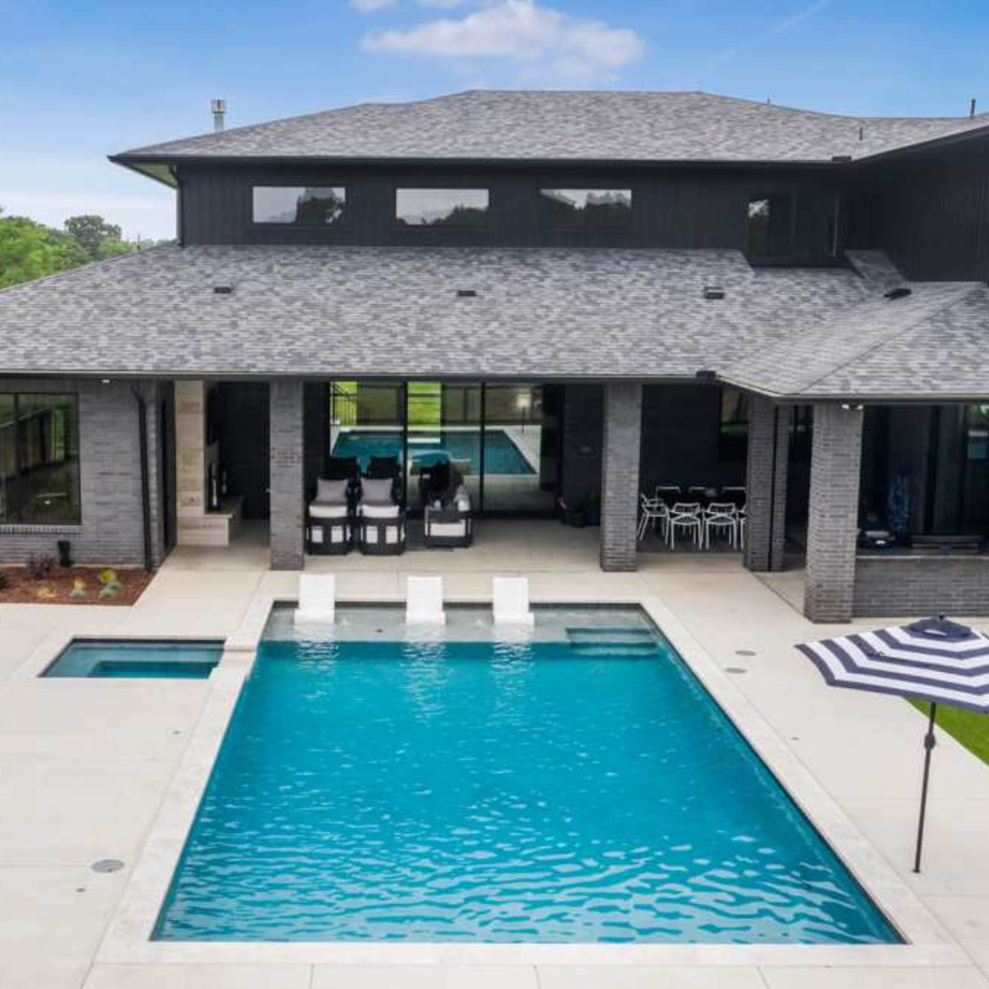A modern house featuring a rectangular swimming pool surrounded by a patio and landscaped greenery.