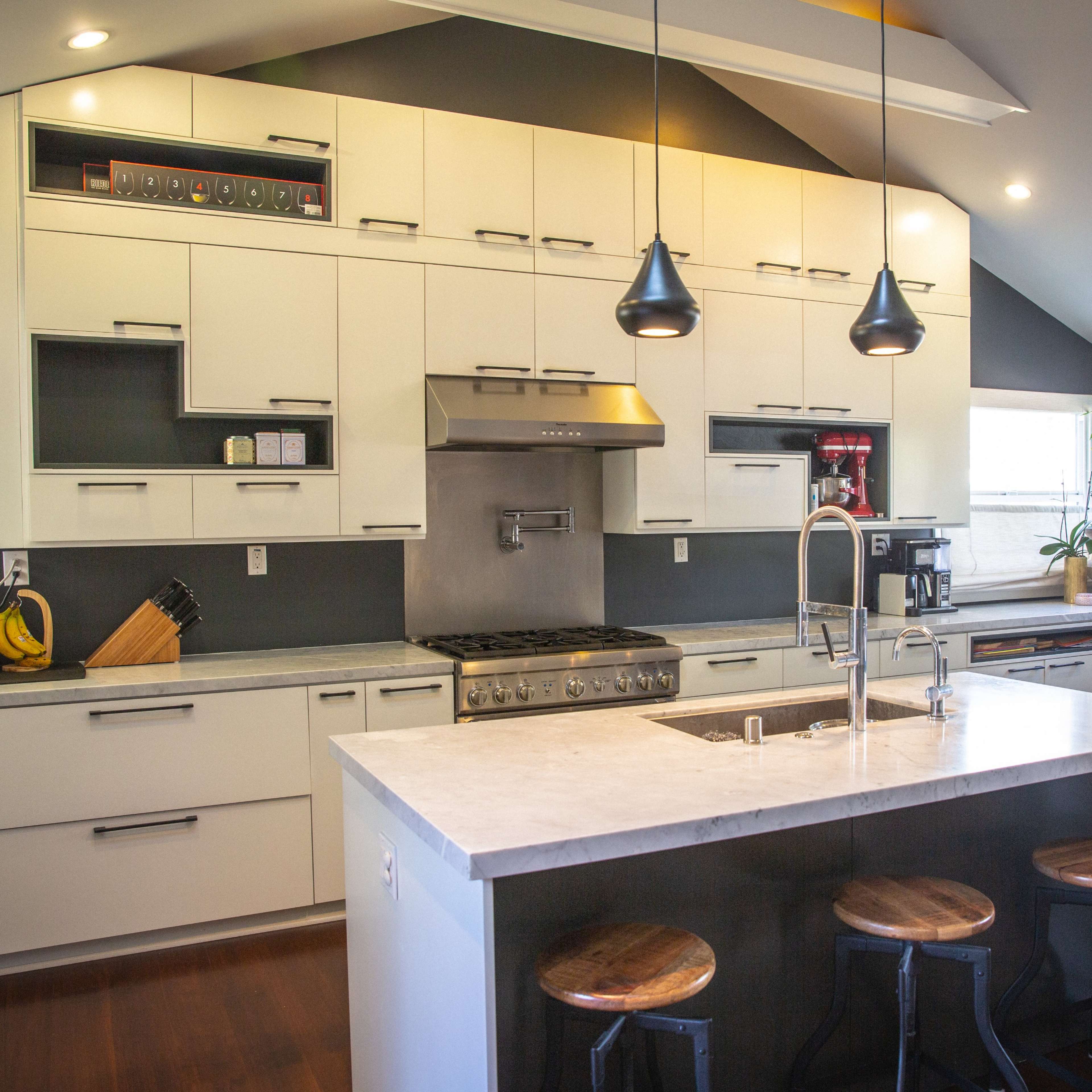 A modern kitchen featuring white cabinetry, stainless steel appliances, and a central island with wooden stools.