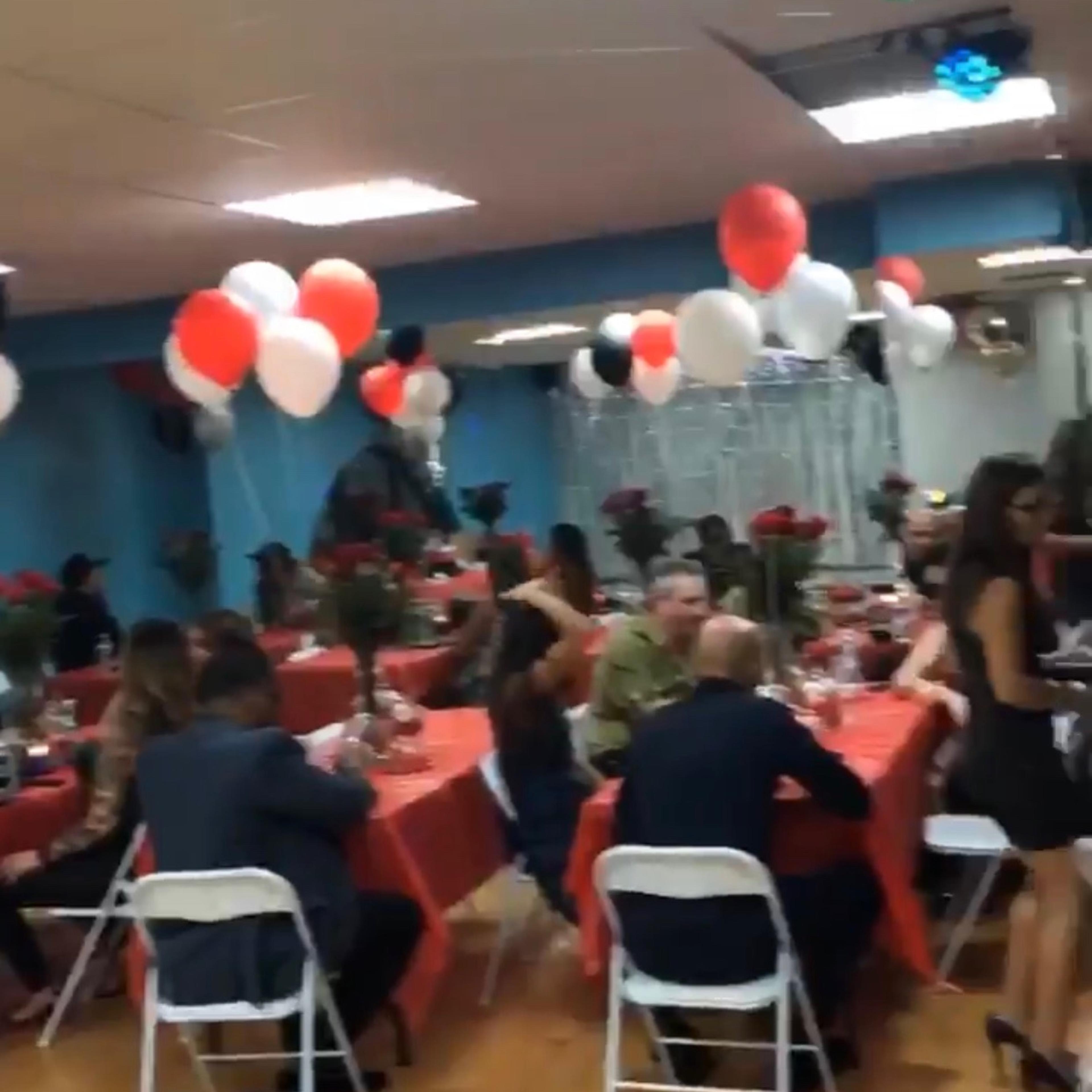 A decorated event space with tables set for a gathering, featuring red and white balloons and flower centerpieces.