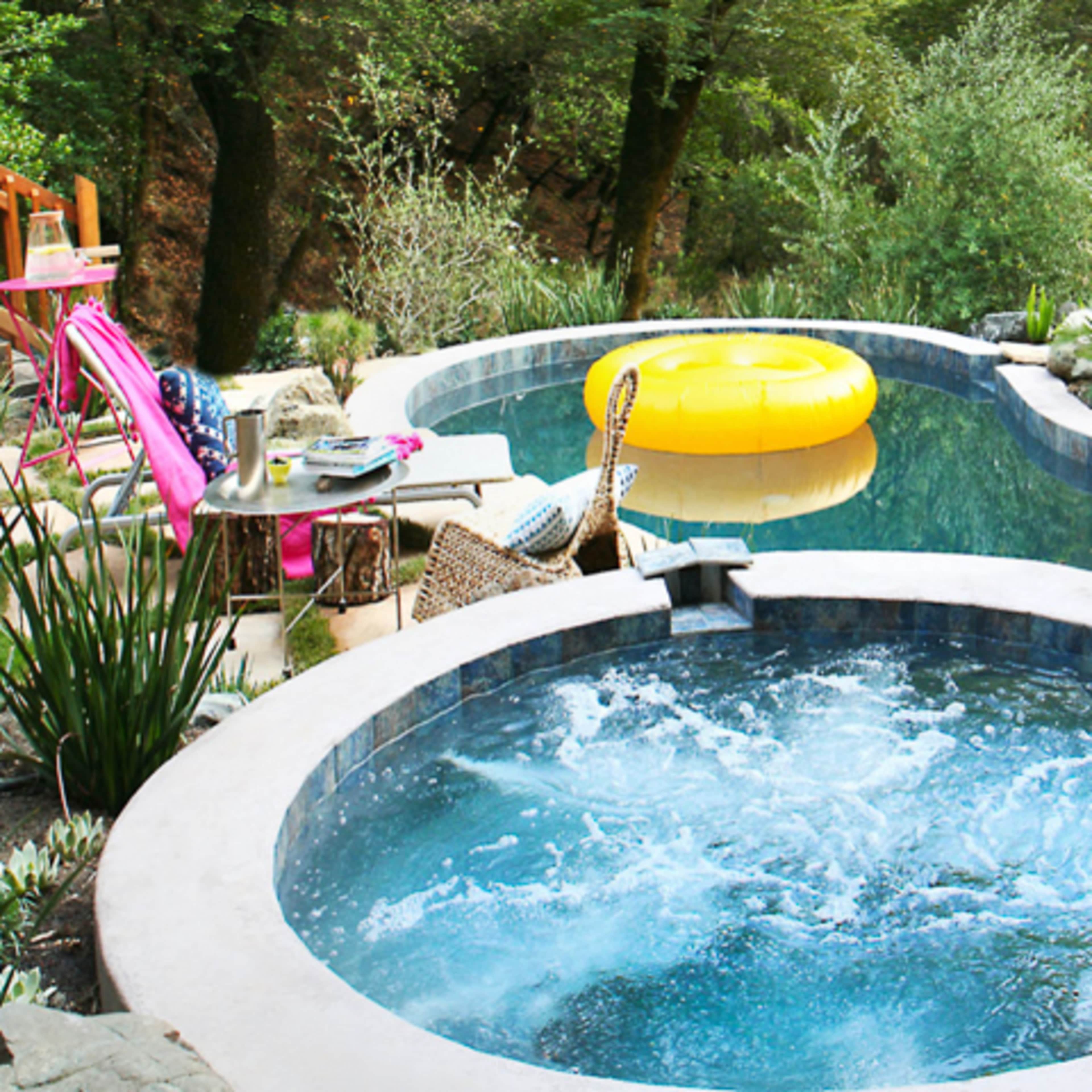 A hot tub bubbles next to a swimming pool surrounded by greenery and a large yellow inflatable float.