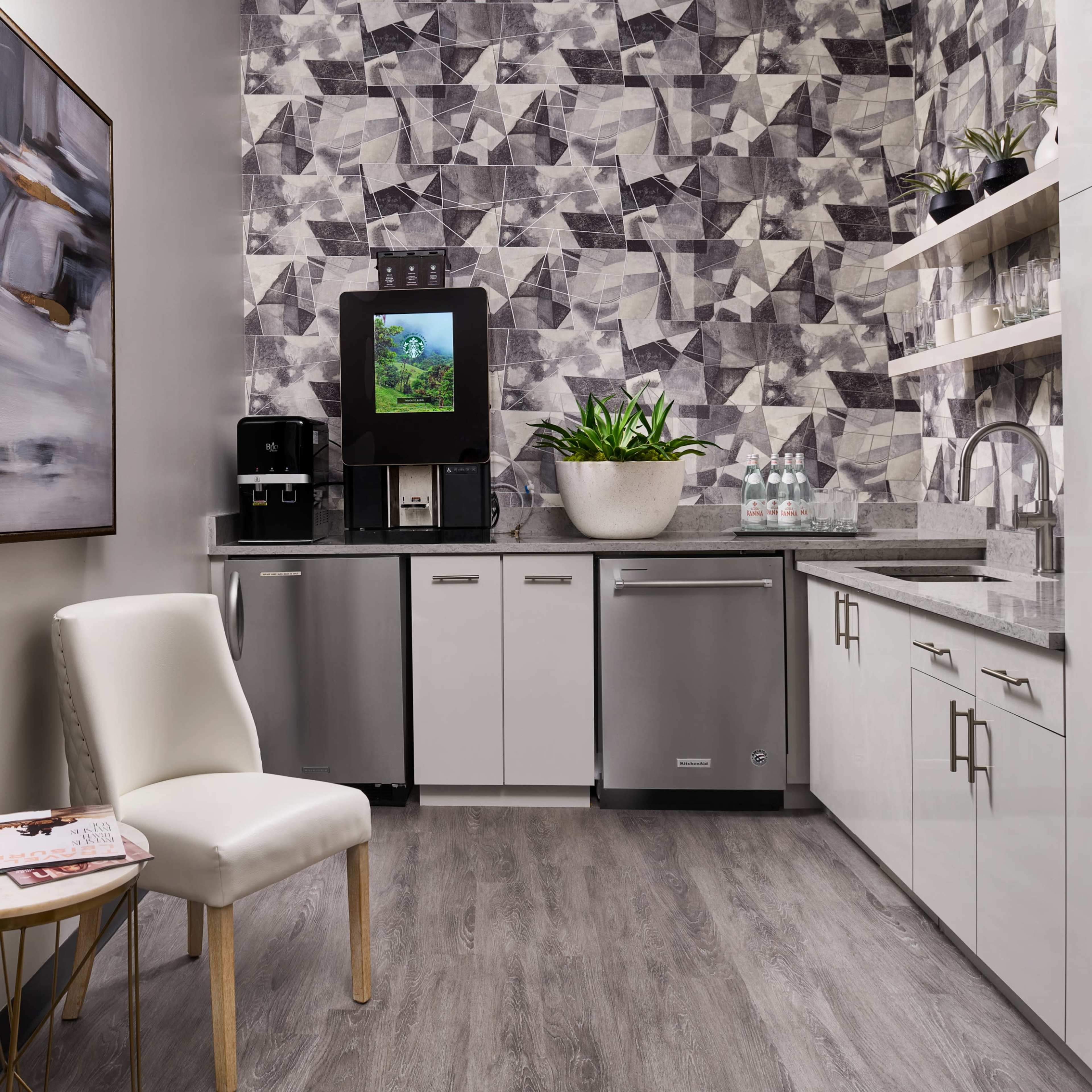 A modern kitchenette with a geometric-patterned wall, a water dispenser, and a small seating area.