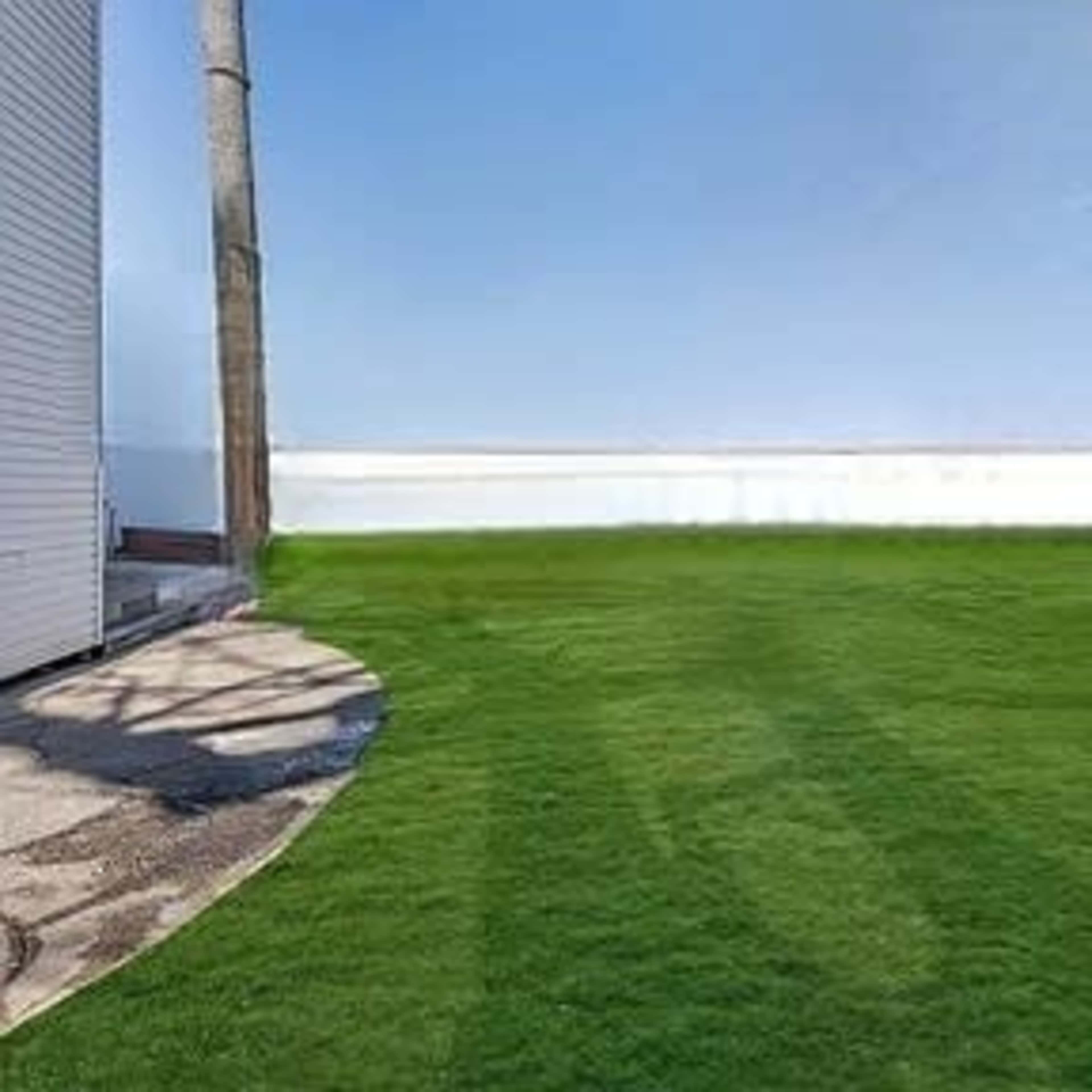 A well-maintained green lawn adjacent to a white structure under a clear blue sky.