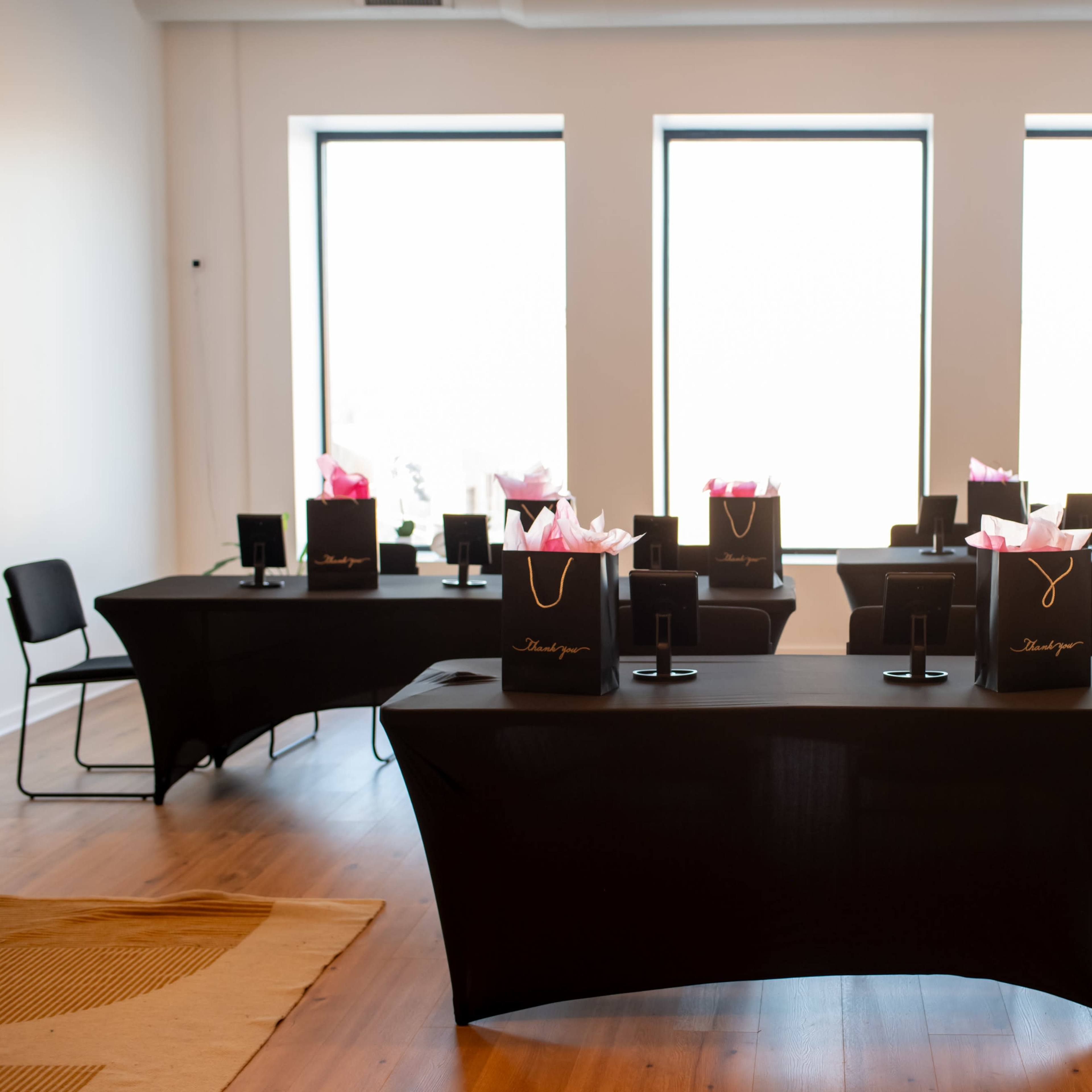 A spacious room with several tables draped in black cloth, each adorned with gift bags and set up for an event.