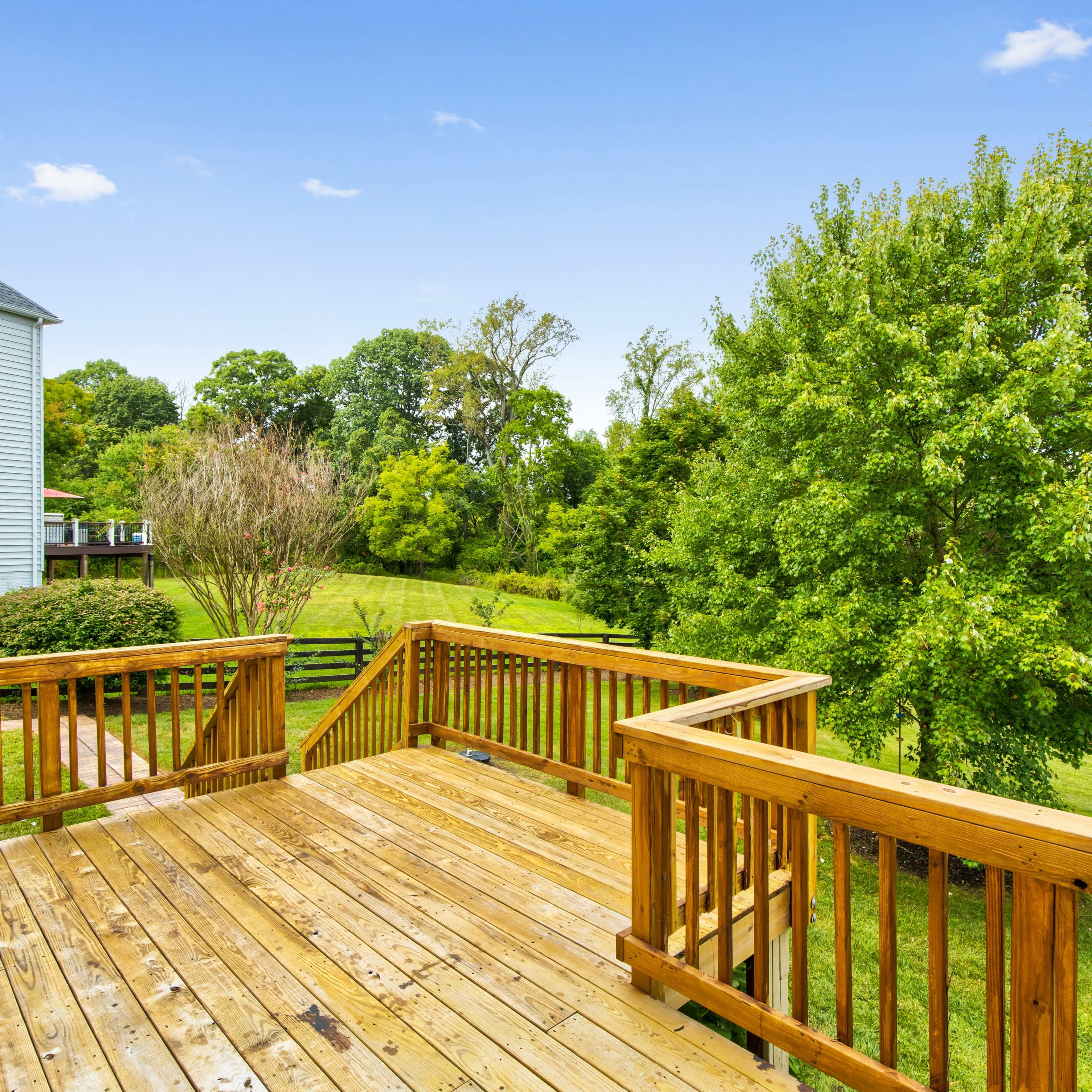 A wooden deck overlooks a grassy yard with trees in the background.