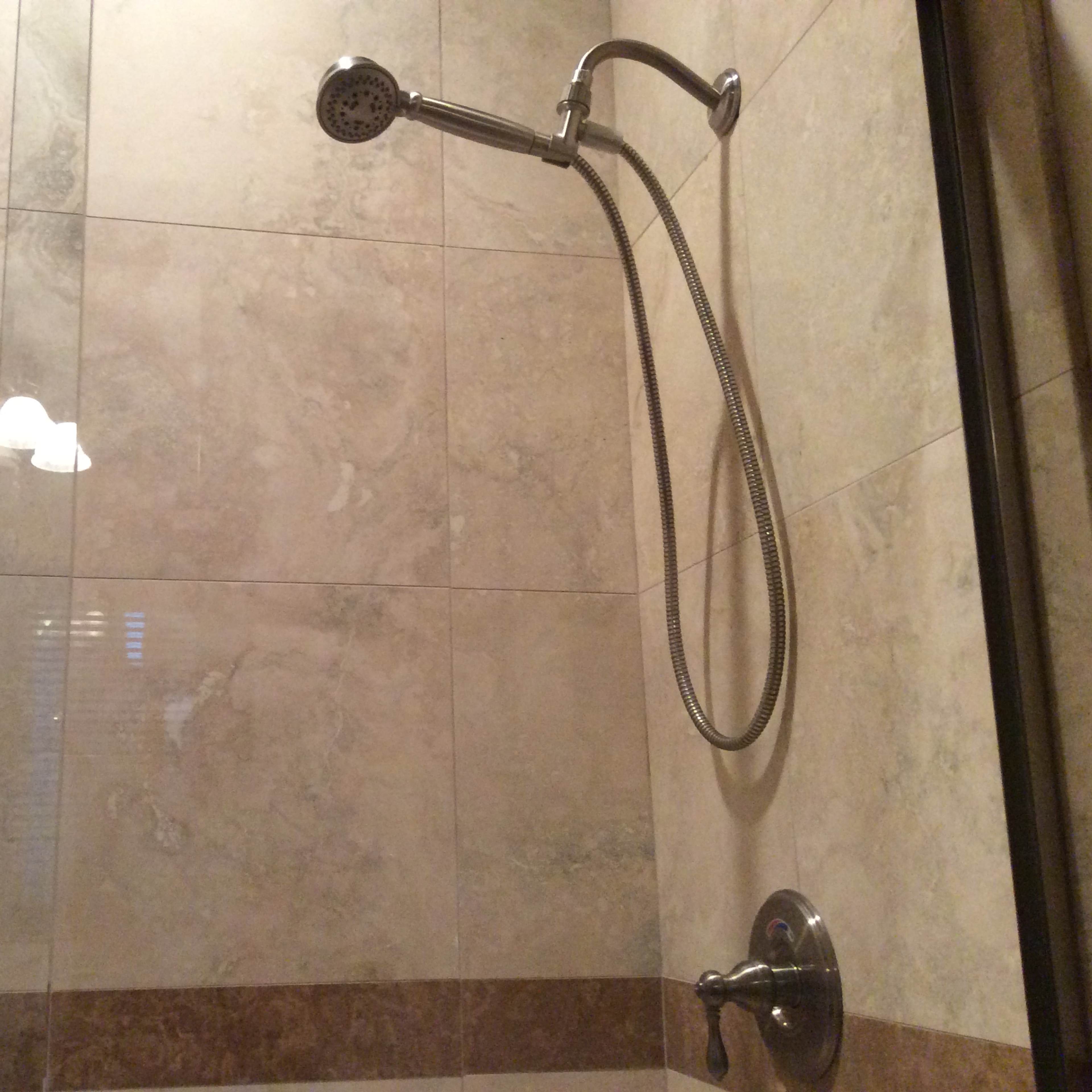 A shower with a handheld showerhead mounted on a tiled wall.