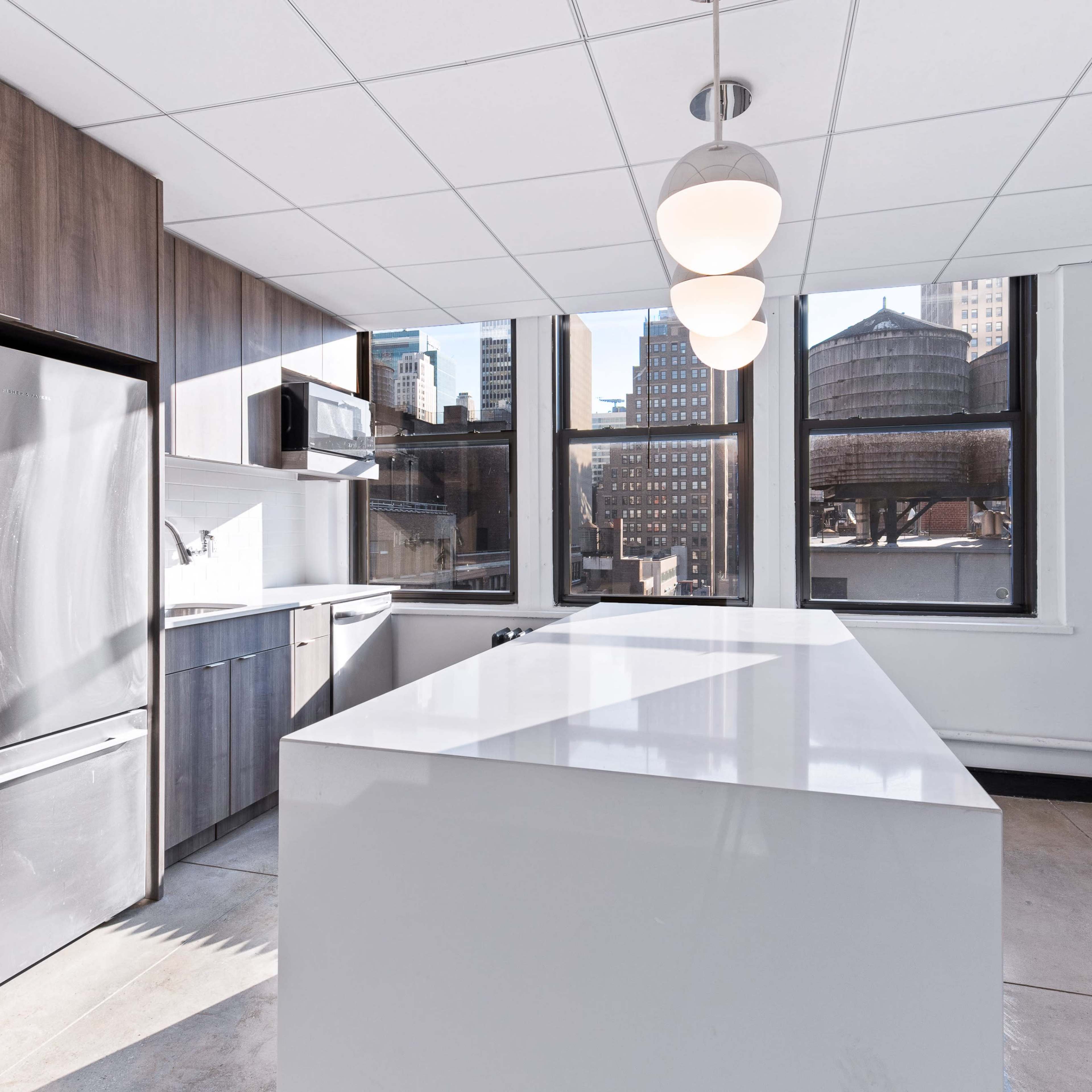 A modern kitchen with a large island, stainless steel appliances, and multiple windows overlooking a cityscape.