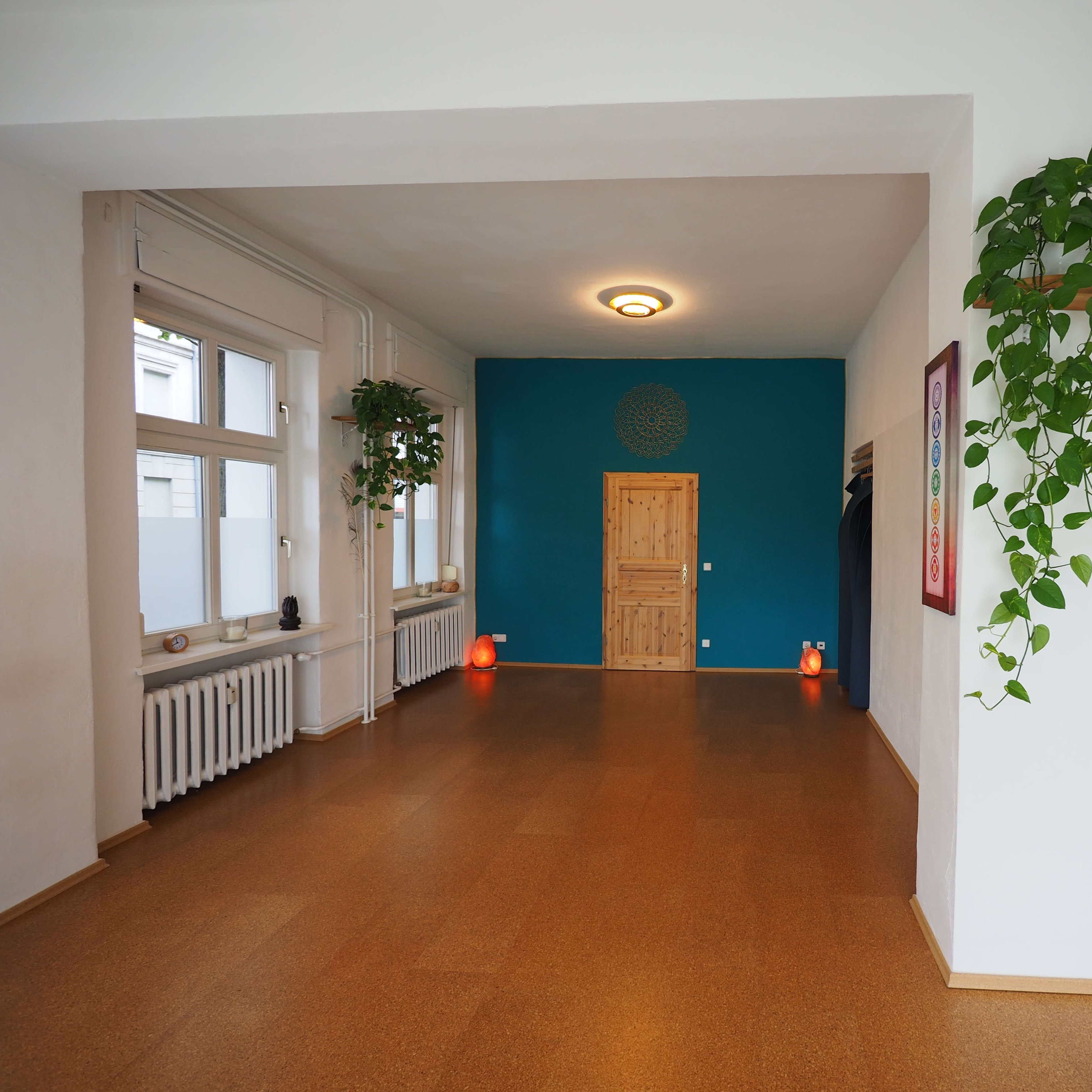 A spacious, well-lit room with a blue accent wall, a wooden door, and potted plants hanging from the ceiling.