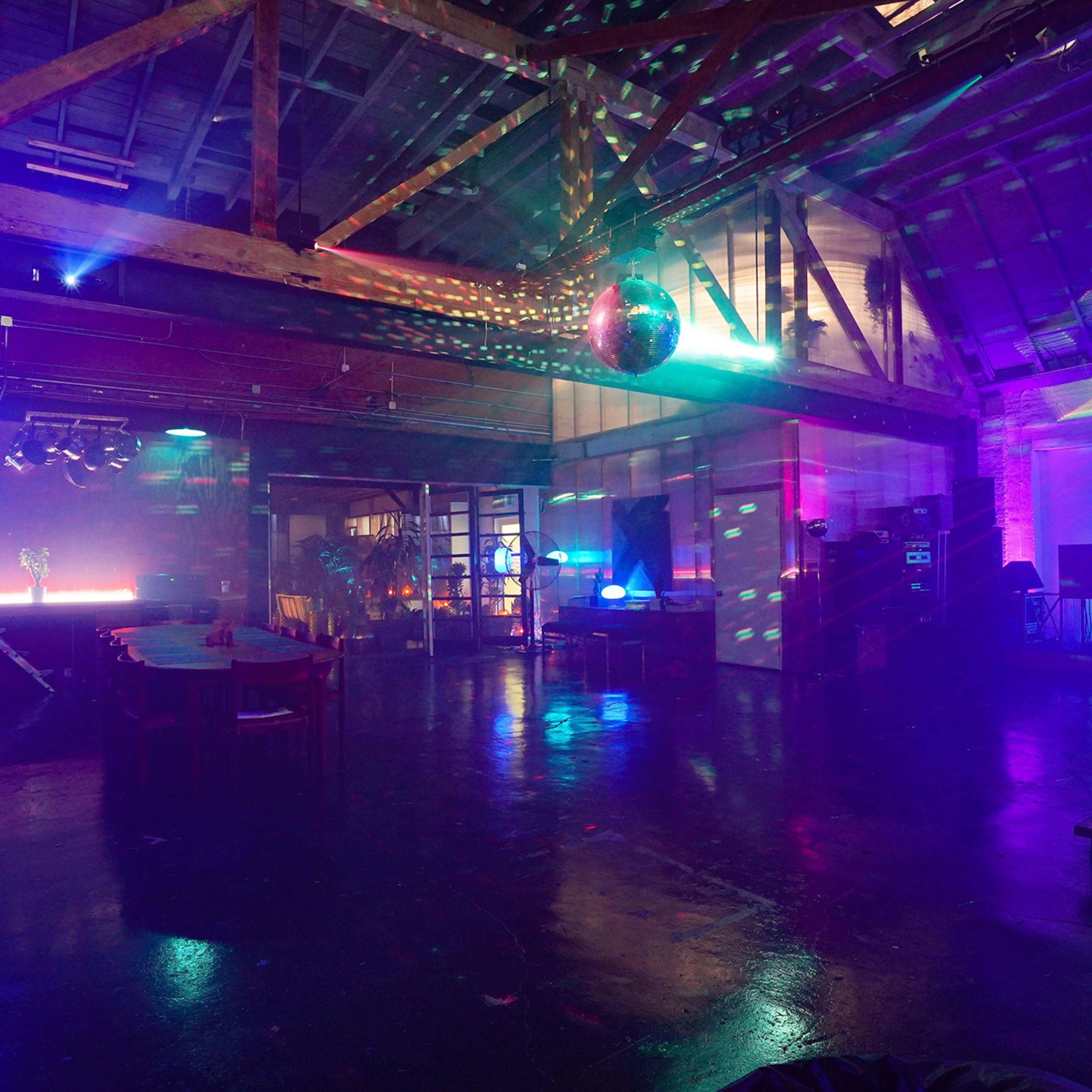 A spacious interior with colorful lighting effects, a disco ball, and various event setups in a warehouse-like venue.