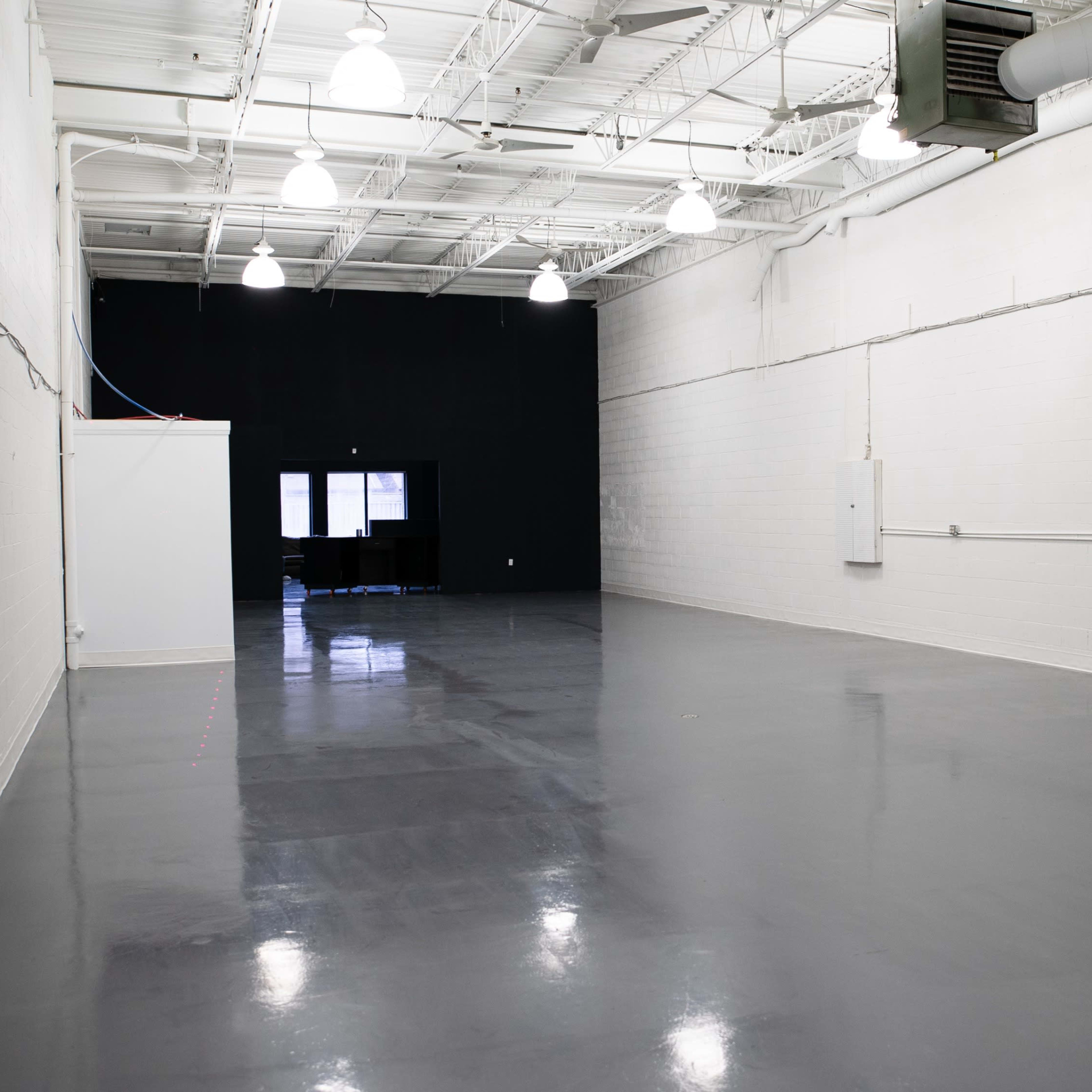 A large, empty indoor space with white walls, a polished gray floor, and a black wall at one end.