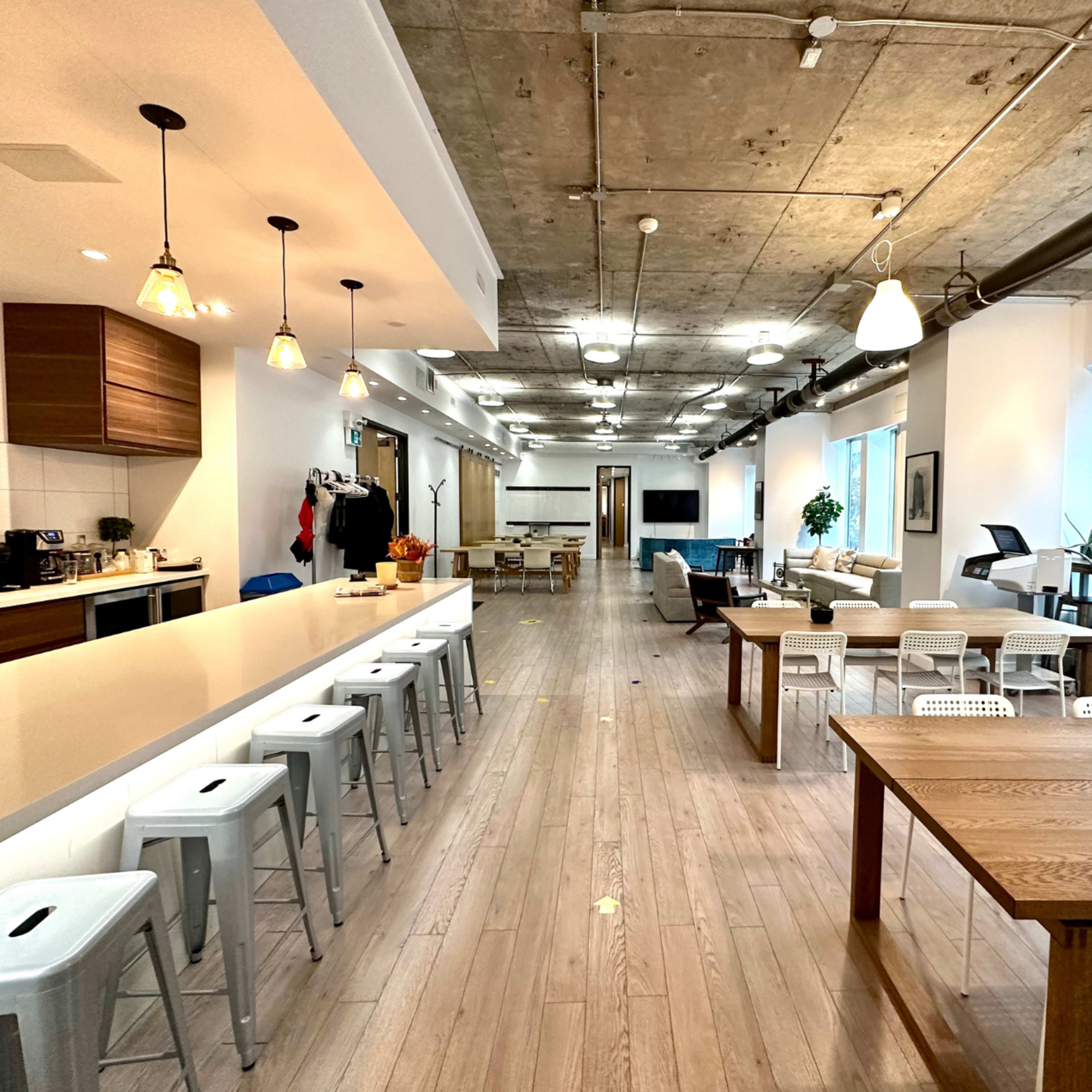 A modern open office space with a long countertop bar, seating areas, and large windows.